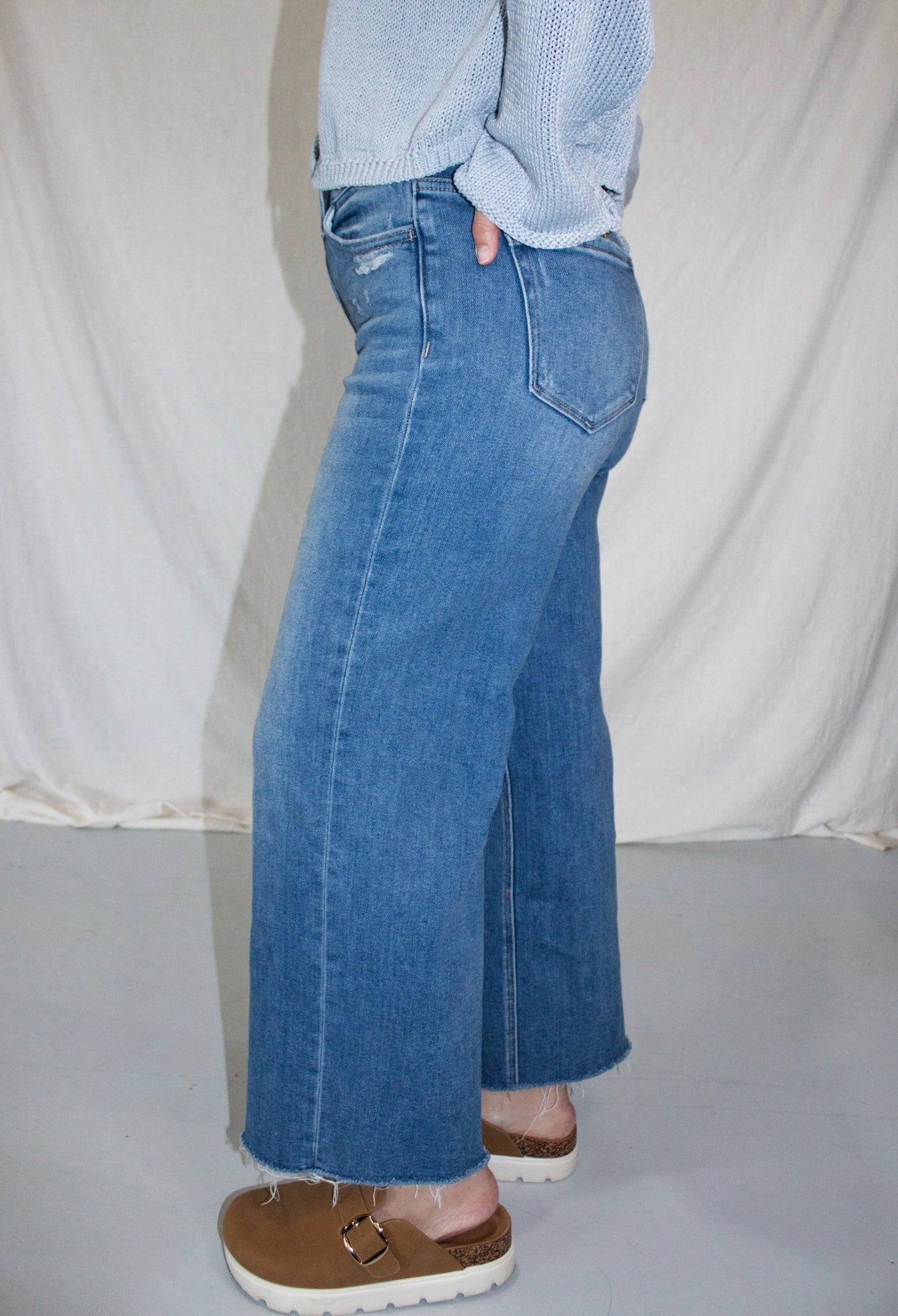 Person wearing blue jeans and a light blue sweater against a plain background