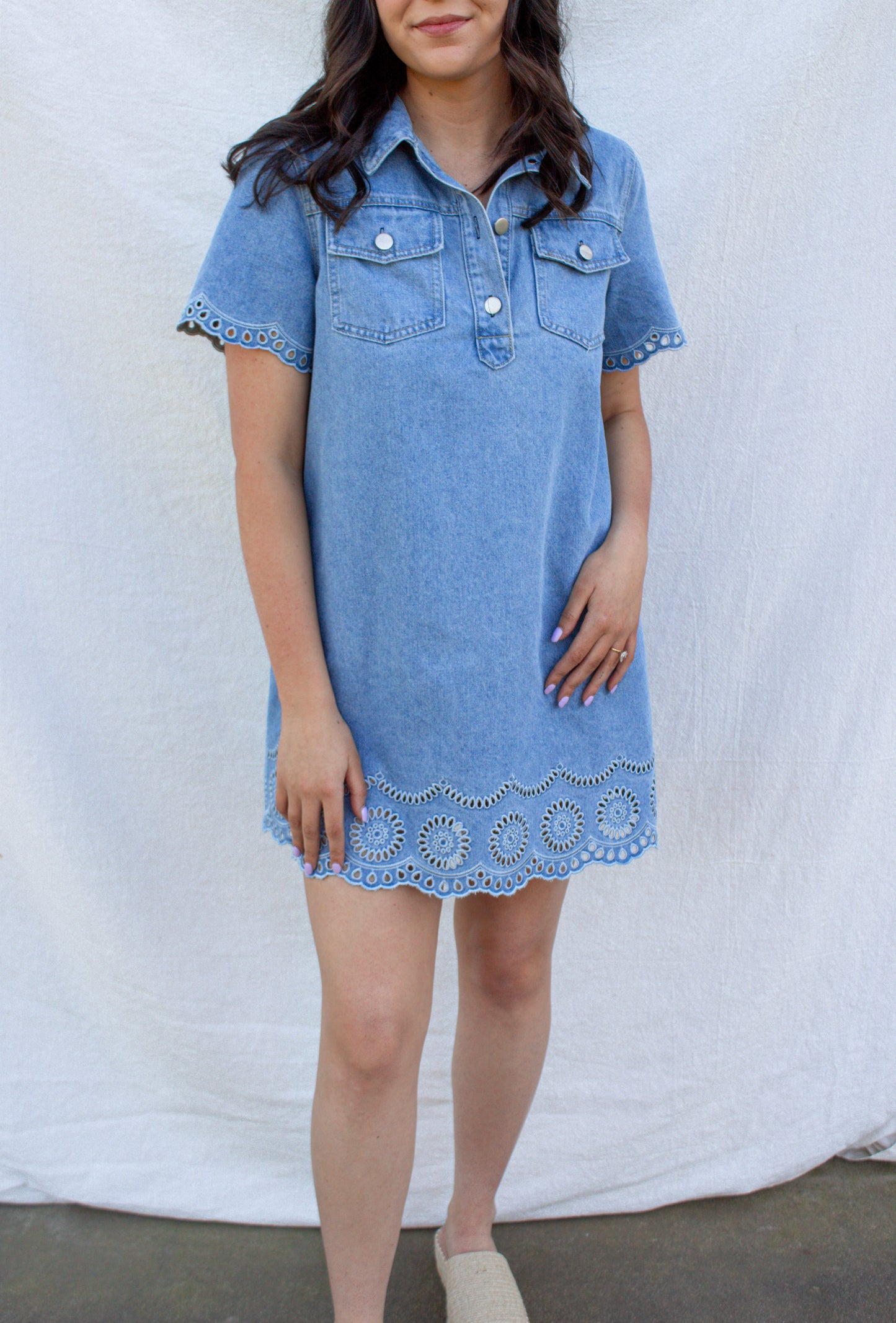 Woman wearing a blue denim dress with lace trim against a white background
