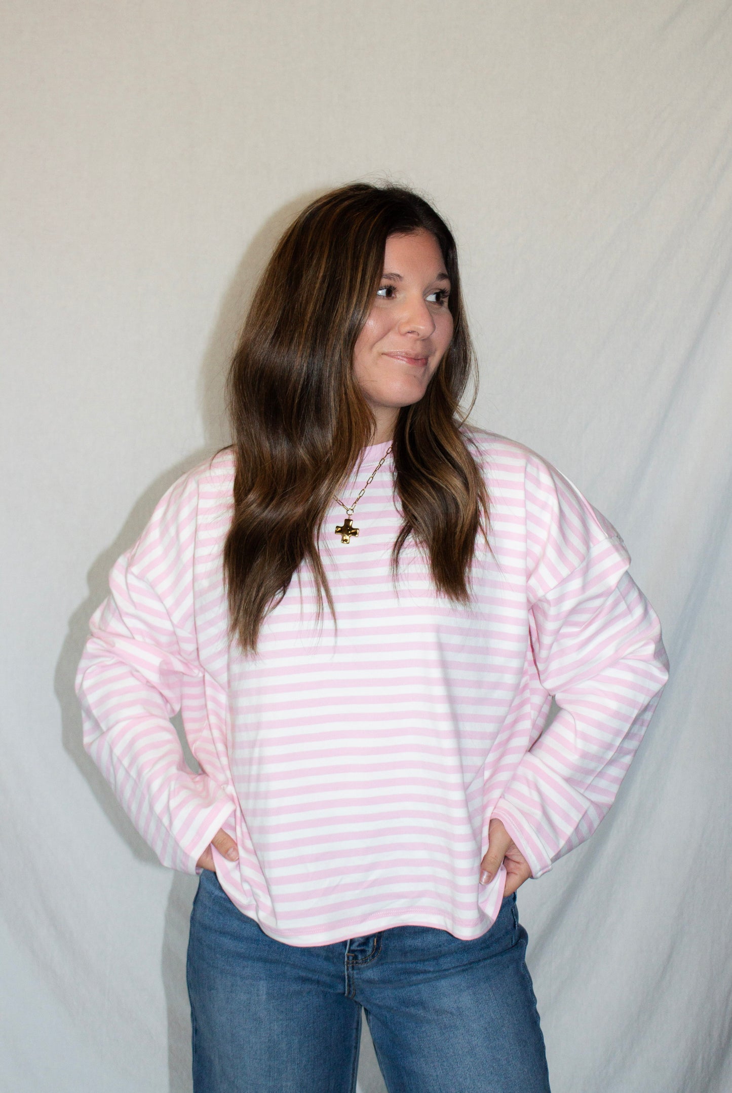 Person wearing a pink and white striped sweater and blue jeans against a plain background
