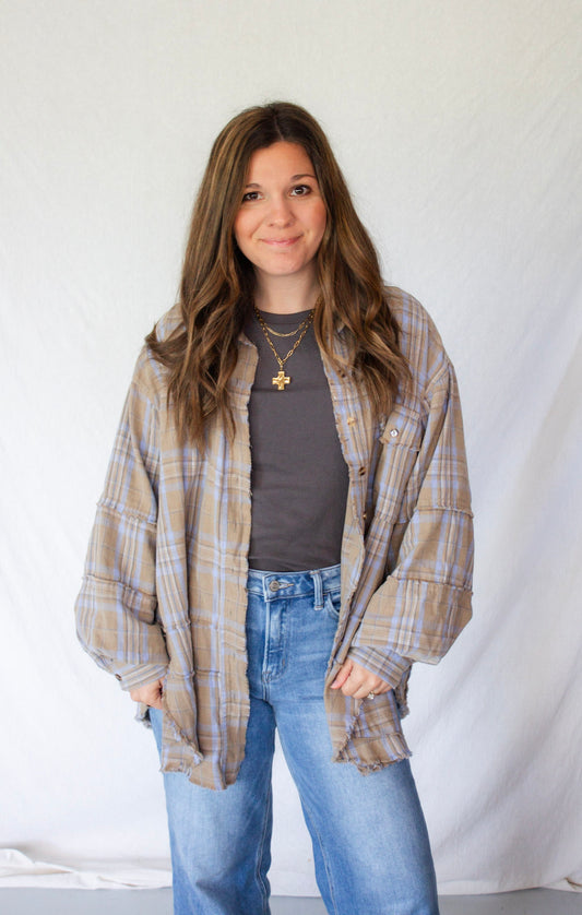 Woman wearing a plaid shirt over a gray top and blue jeans against a white background