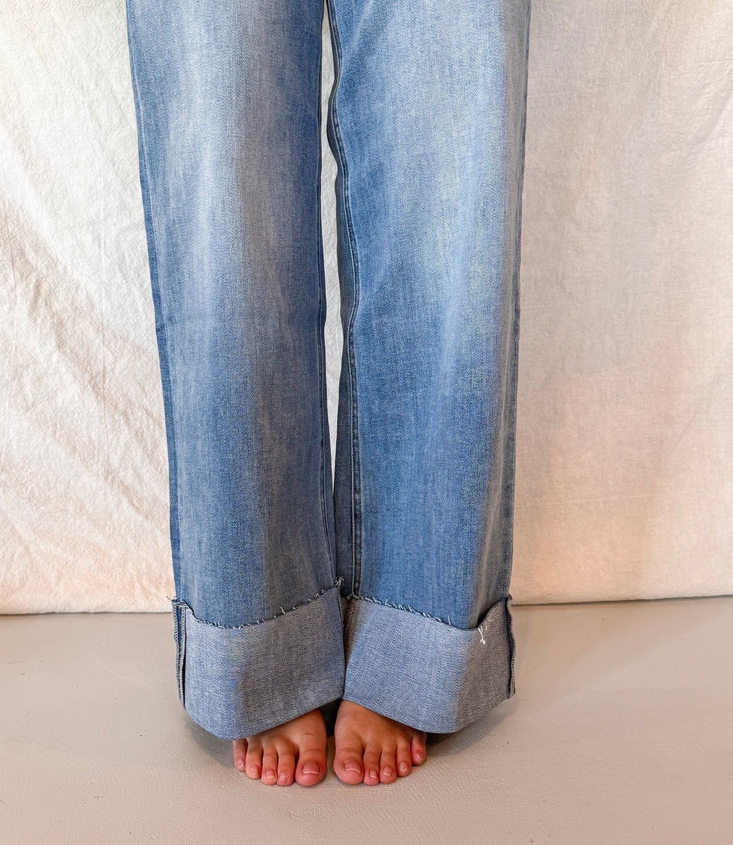Blue jeans with cuffed ankles on a neutral background