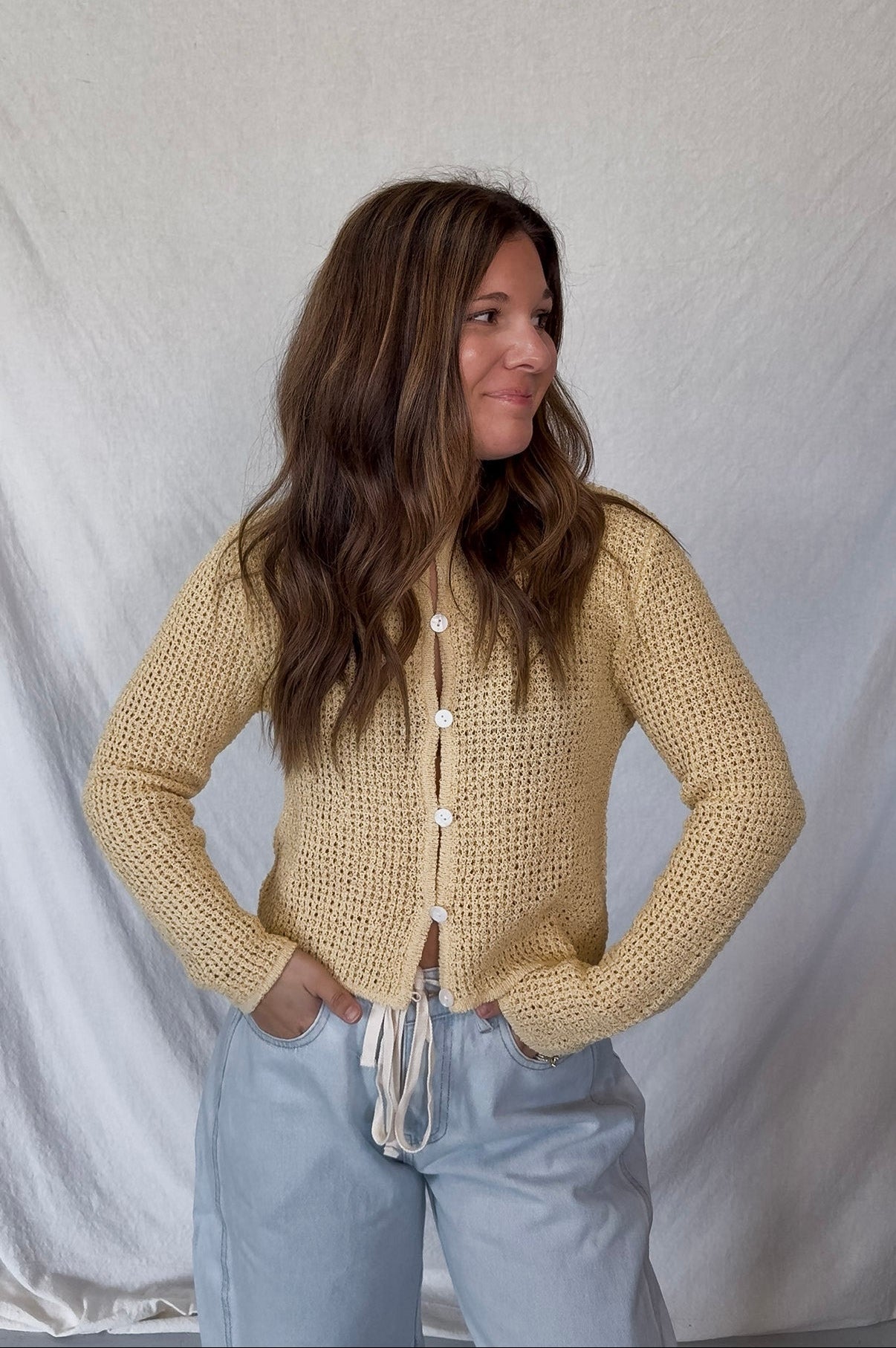 Woman wearing a beige knitted cardigan and light blue jeans against a white background