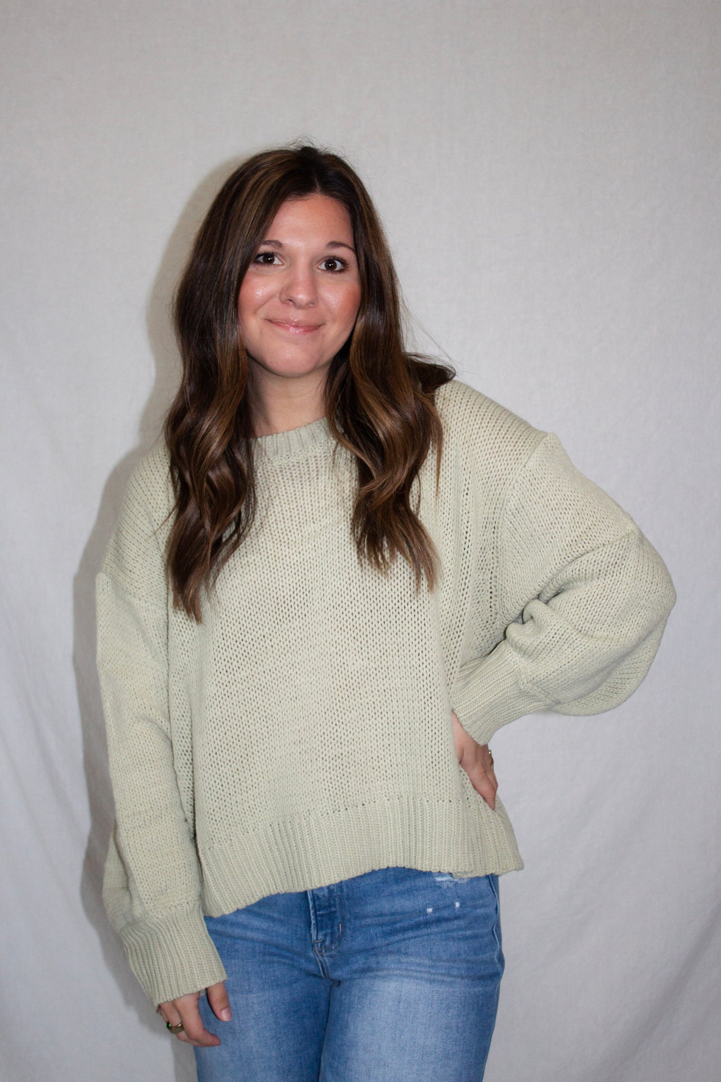 Woman wearing a light green sweater and blue jeans against a plain background