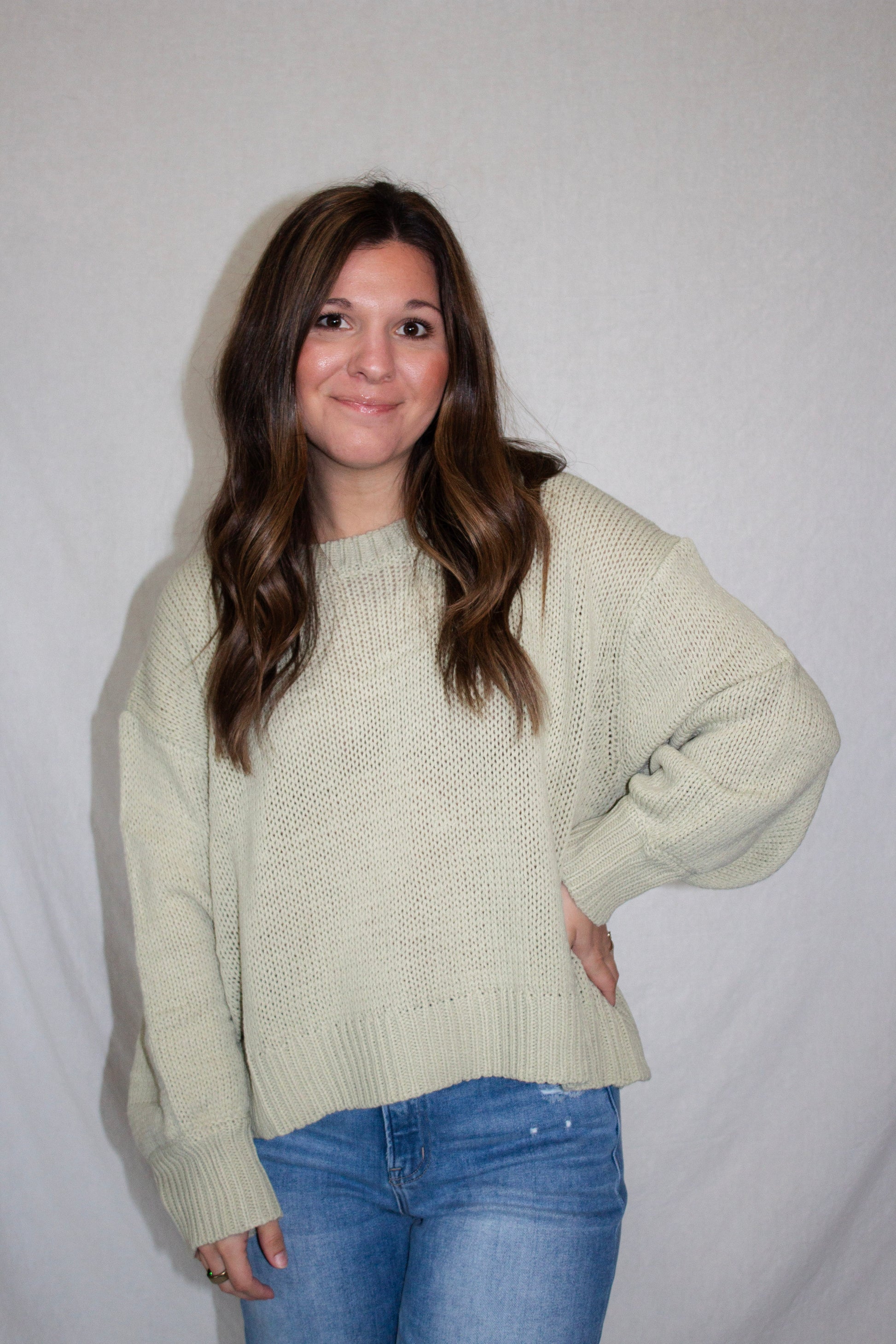 Woman wearing a light green sweater and blue jeans against a plain background