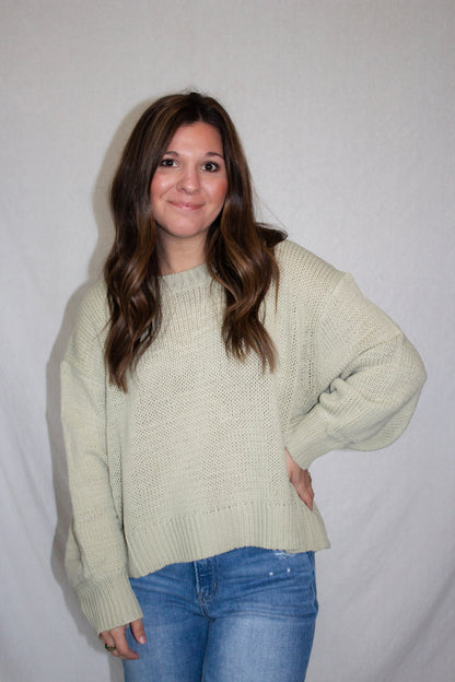 Woman wearing a light green sweater and blue jeans against a plain background