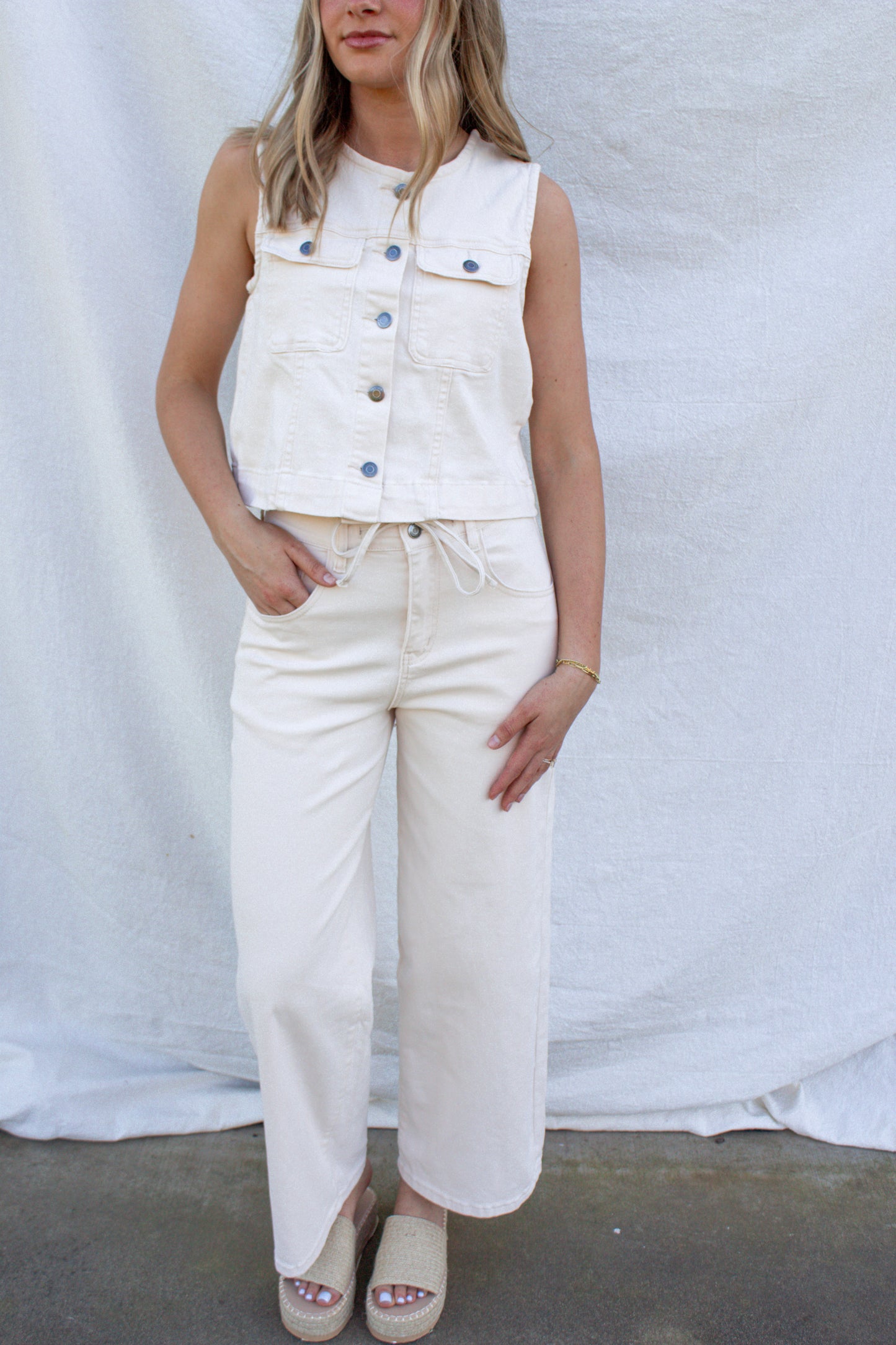 Woman wearing a white sleeveless vest over a white top and pants against a white background