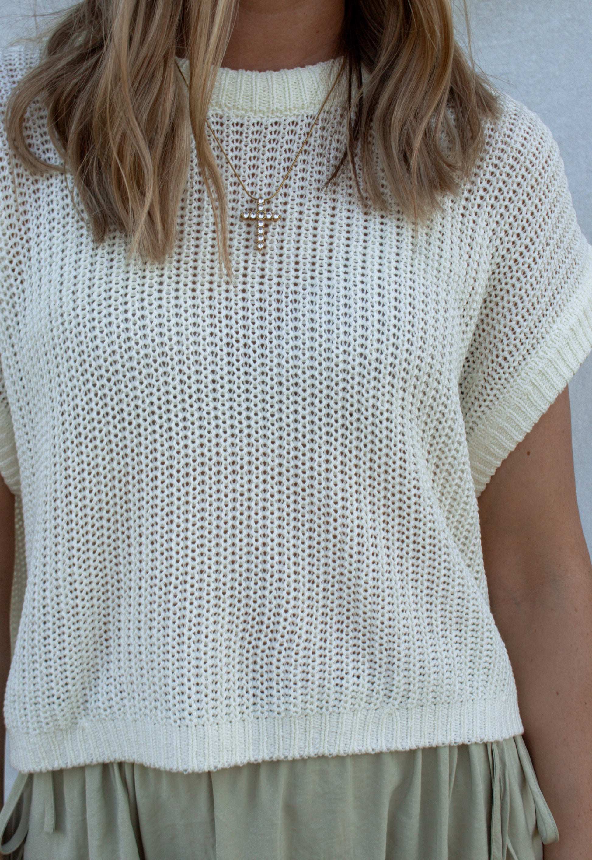 Person wearing a white knit top with short sleeves against a neutral background