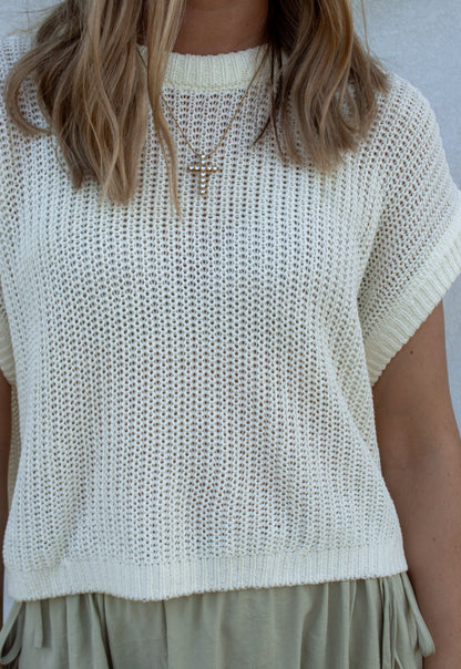 Person wearing a white knit top with short sleeves against a neutral background