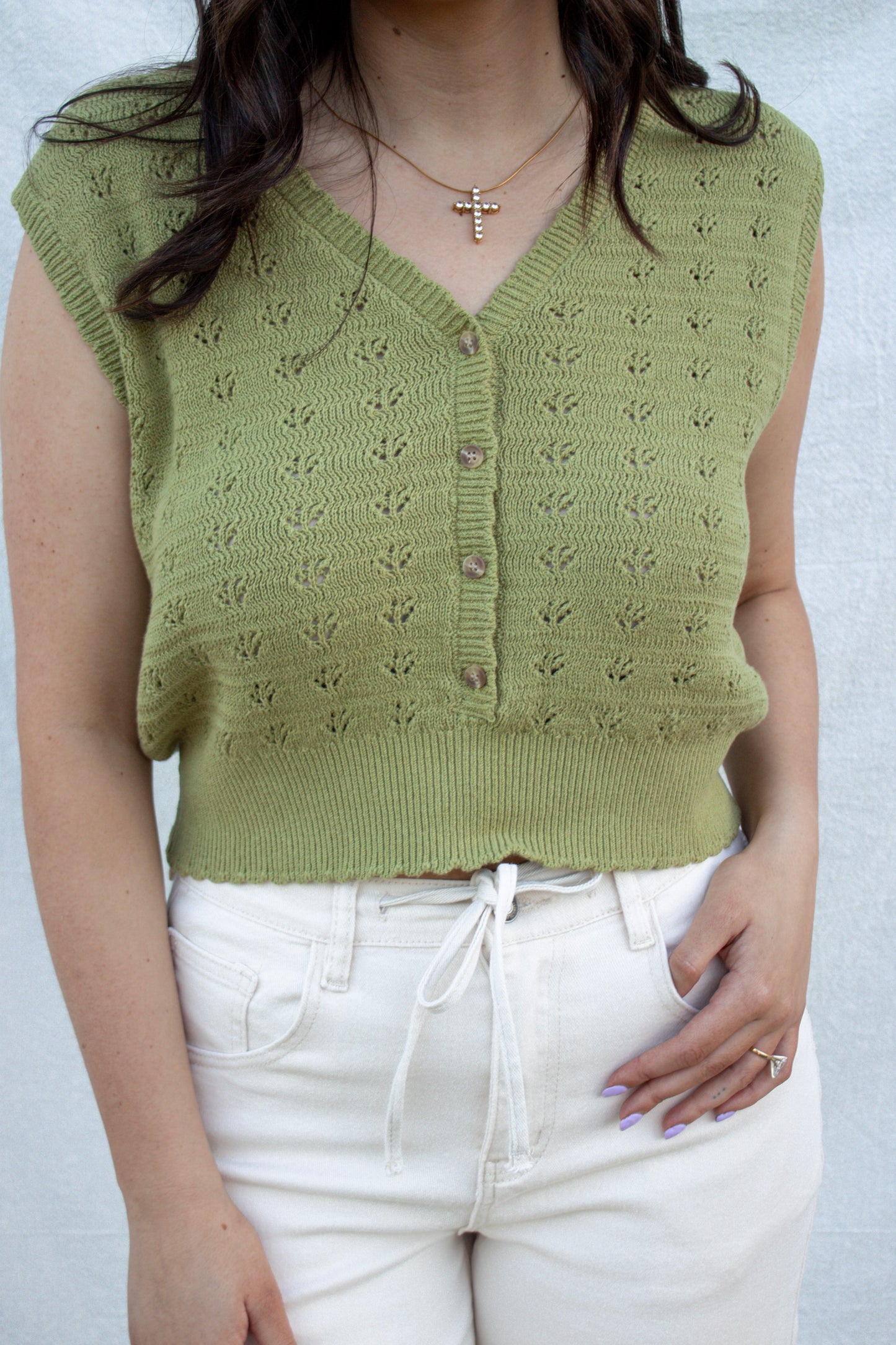Person wearing a green knitted vest over a white top against a plain background