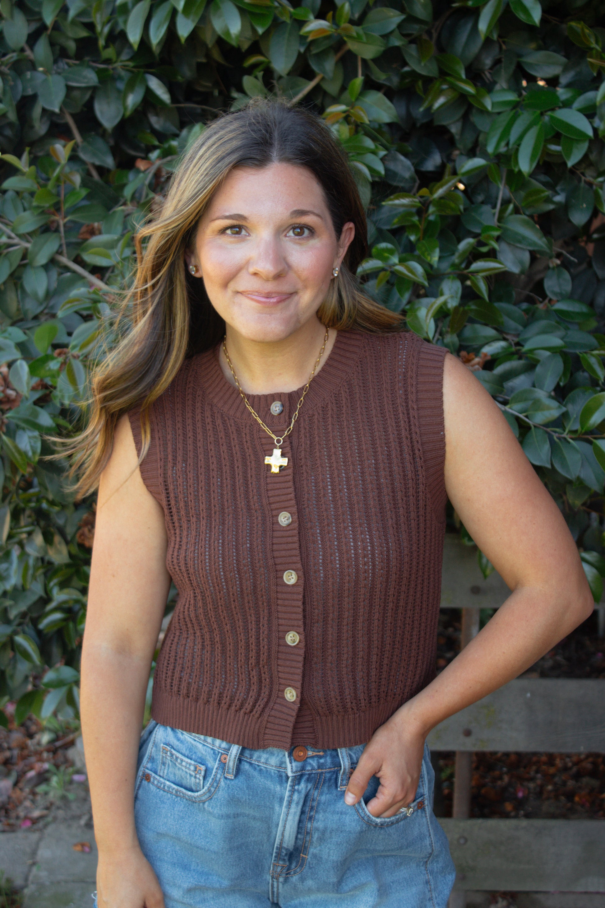 Woman wearing a brown knitted vest with a leafy background