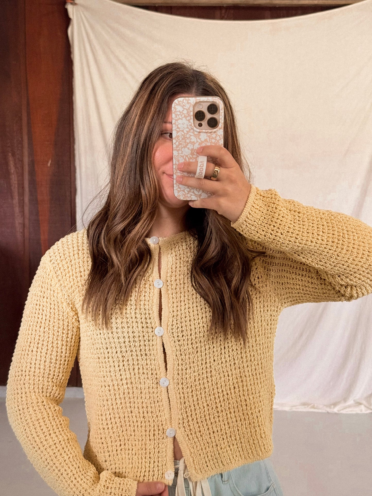 Person wearing a yellow knitted cardigan taking a mirror selfie.