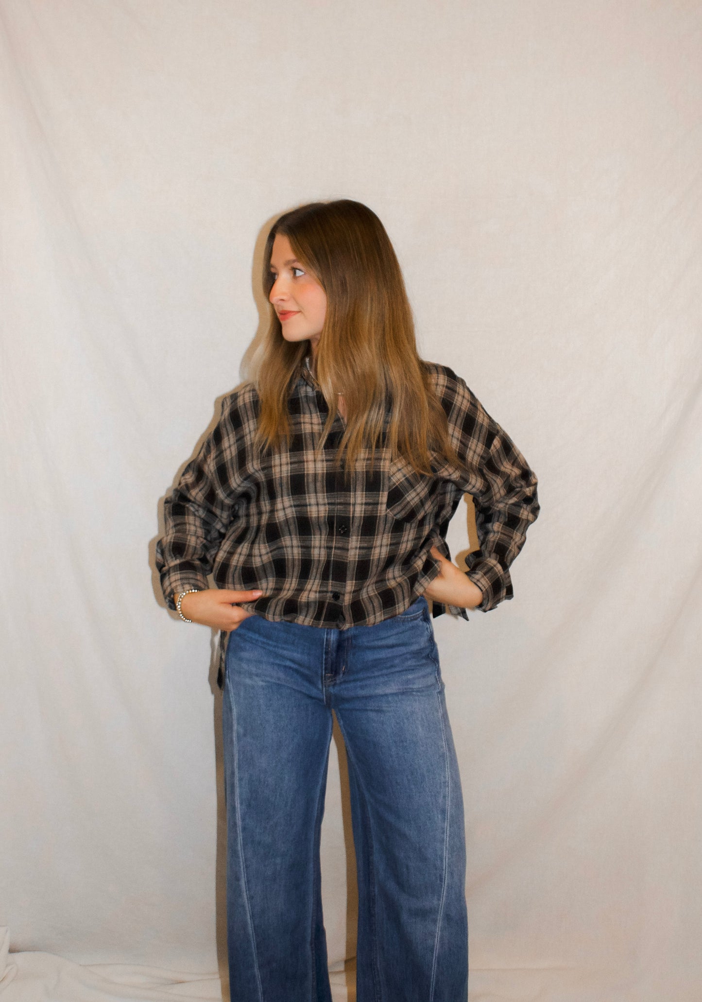 Woman wearing a plaid shirt and blue jeans against a plain background