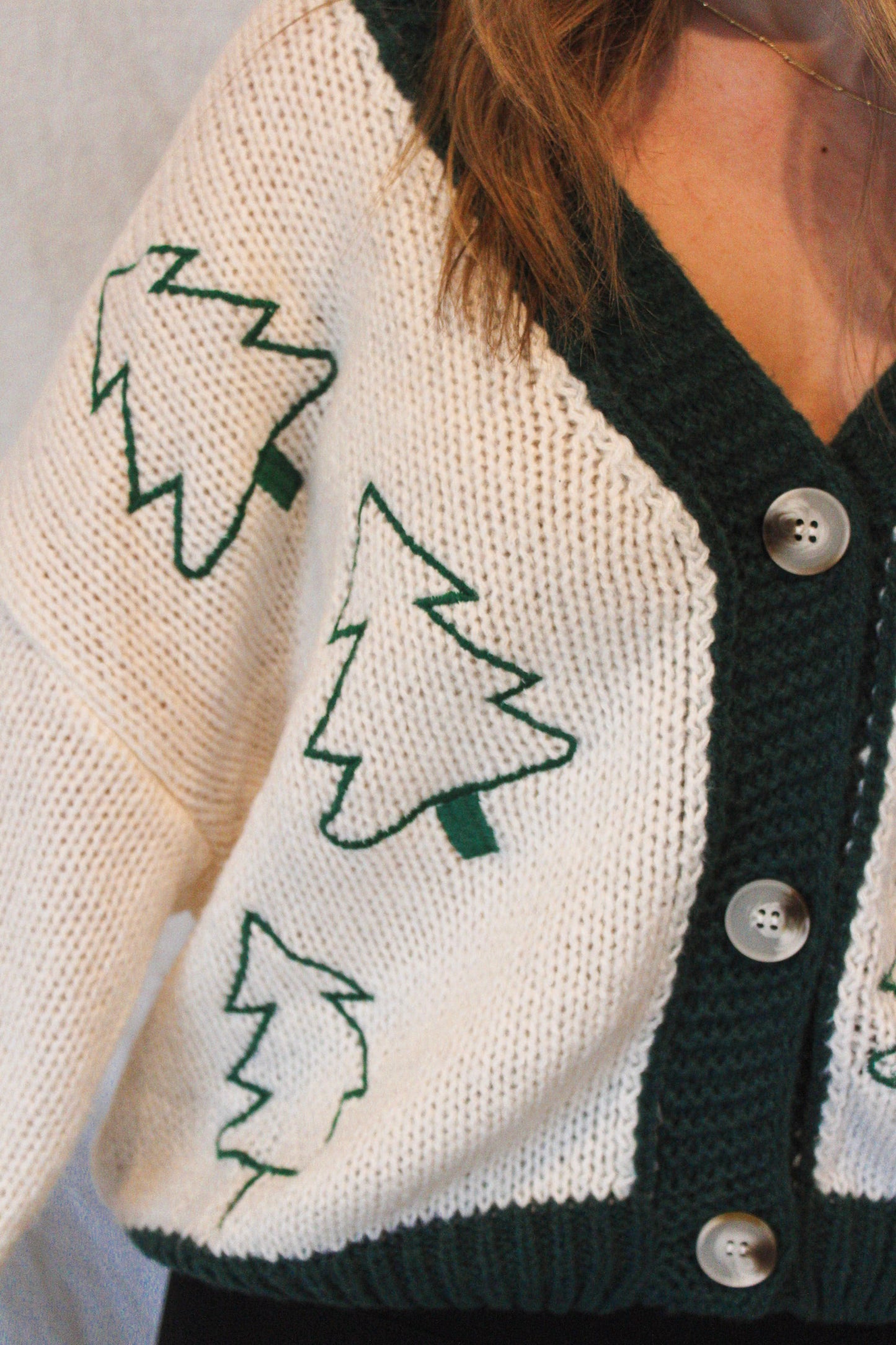 Close-up of a person wearing a cardigan with tree patterns and buttons.