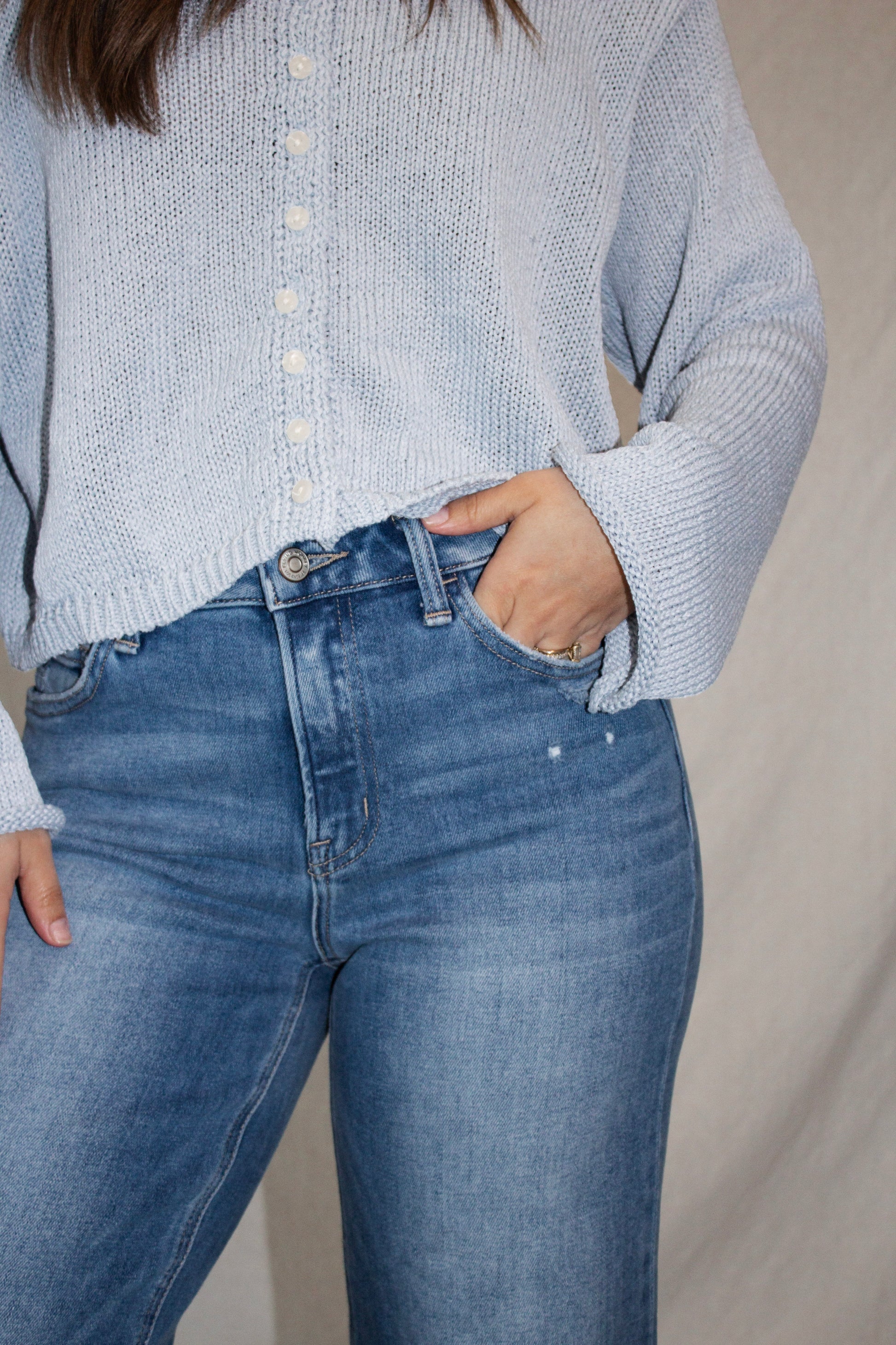 Person wearing a light blue knitted sweater and blue jeans against a neutral background