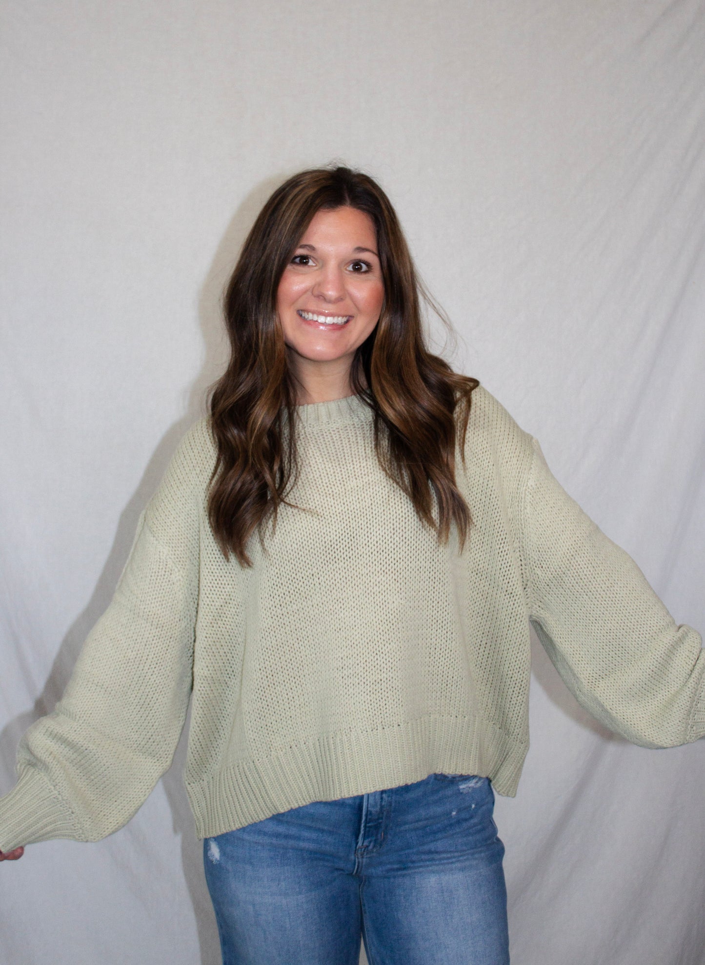 Woman wearing a light green sweater and blue jeans against a white background
