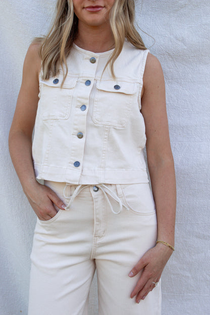 Person wearing a white denim vest over a white shirt with white jeans against a light background