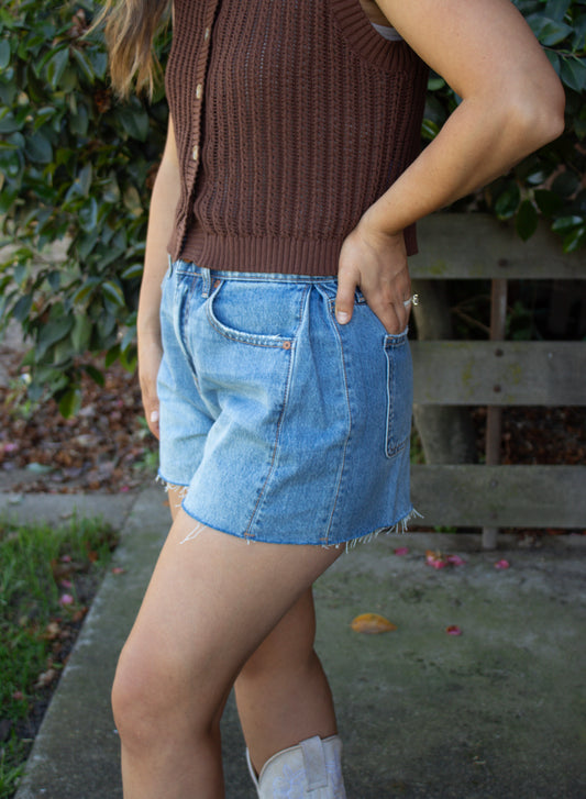 Person wearing a brown ribbed top and denim shorts standing outdoors.