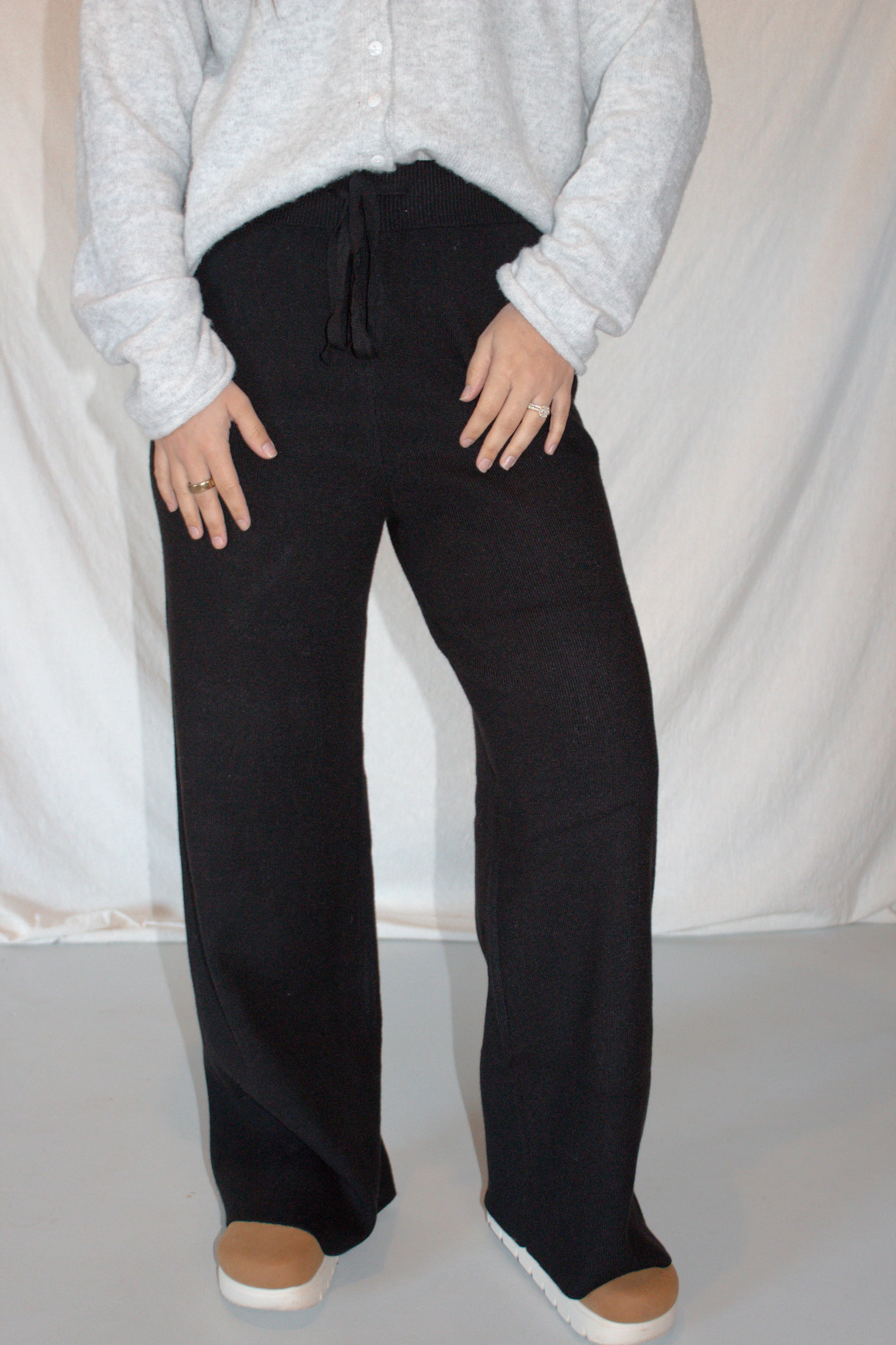 Person wearing black pants and a light gray sweater against a white background
