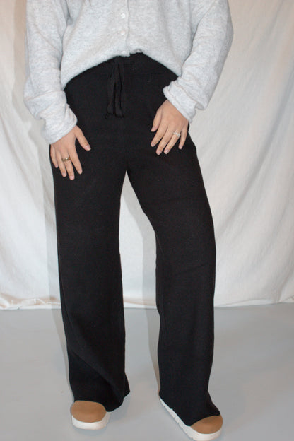 Person wearing black pants and a light gray sweater against a white background