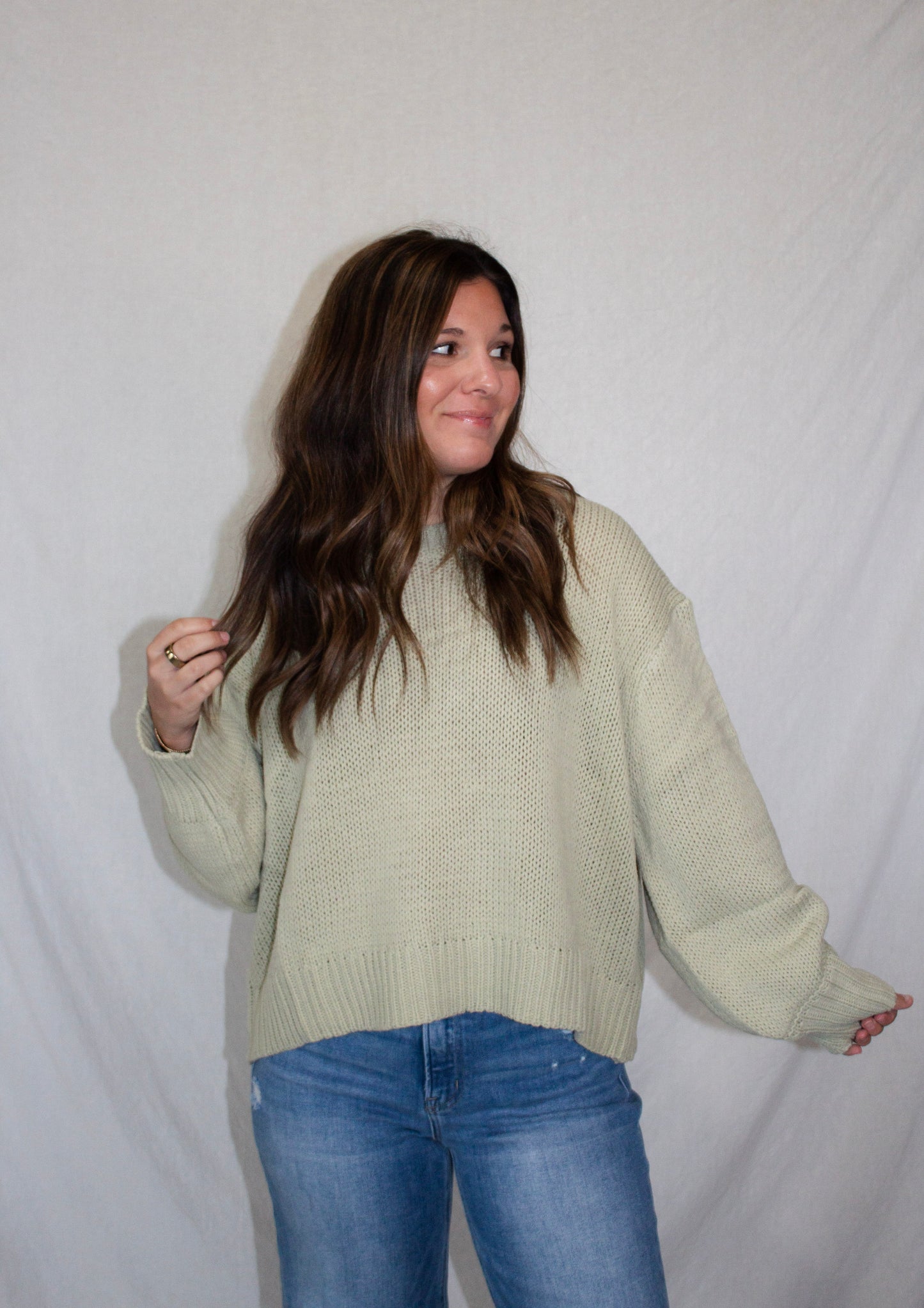 Woman wearing a light green sweater and blue jeans against a white background
