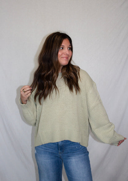 Woman wearing a light green sweater and blue jeans against a white background