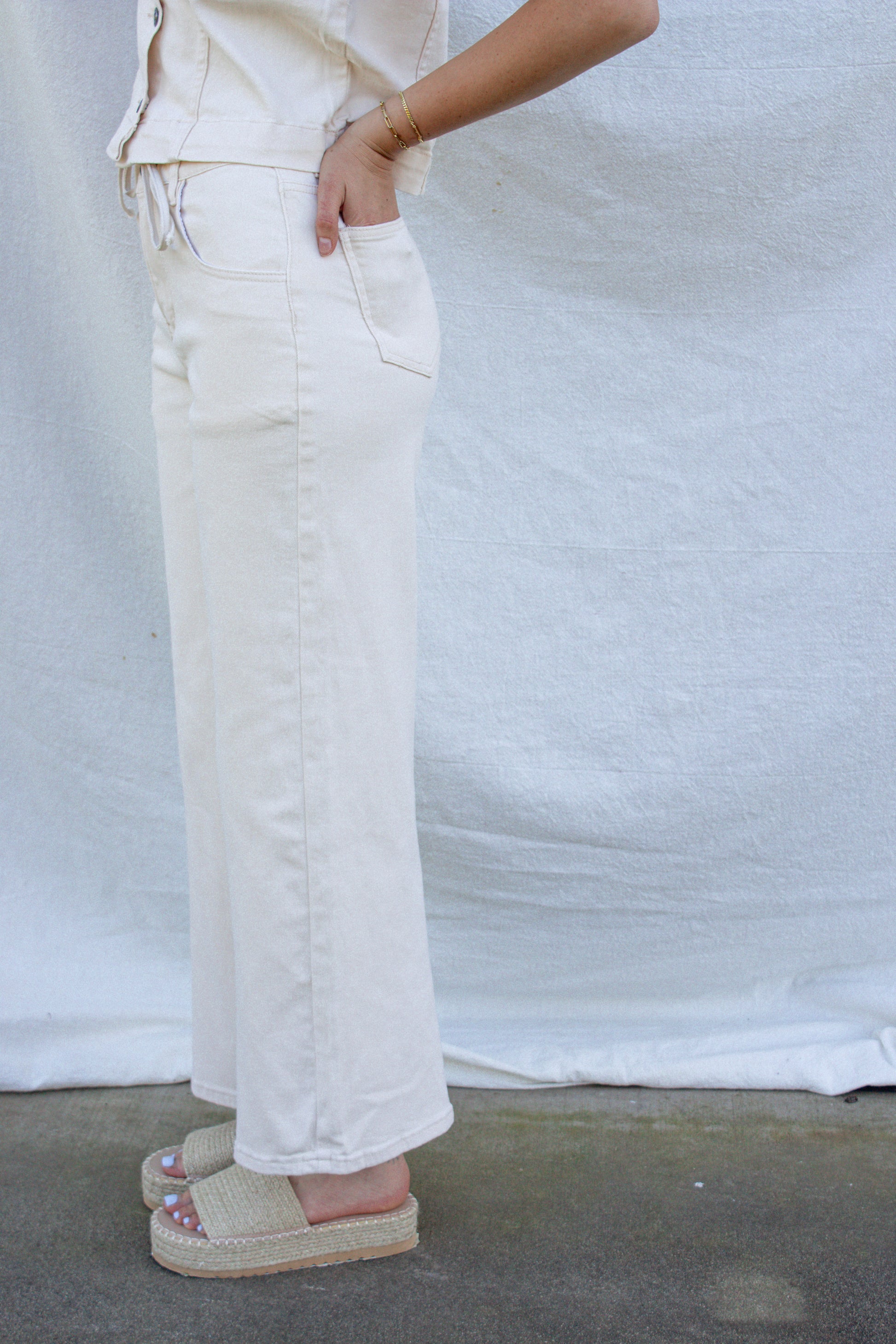 Person wearing white jeans and pink sandals on a plain background