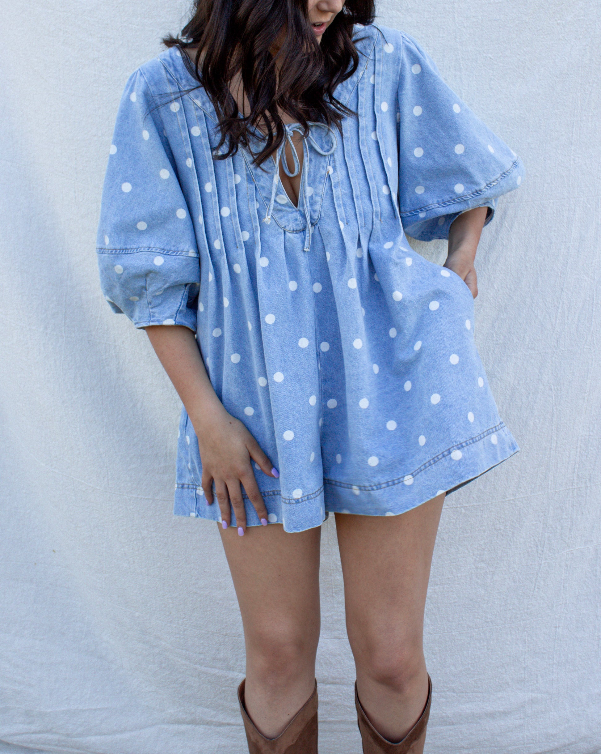 Woman wearing a blue polka dot dress with brown boots against a light gray background