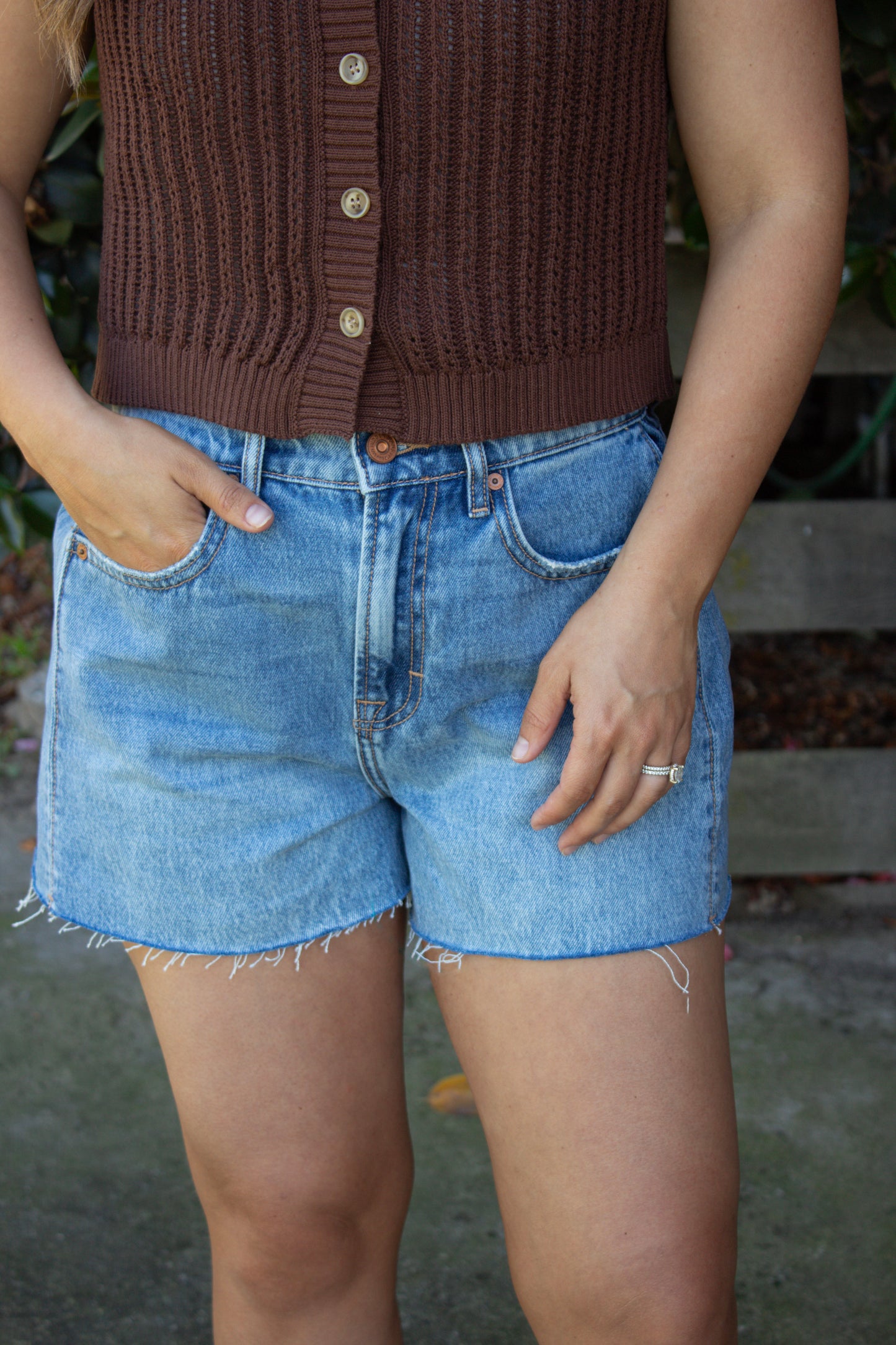 Person wearing a brown knitted vest and blue denim shorts with a blurred background