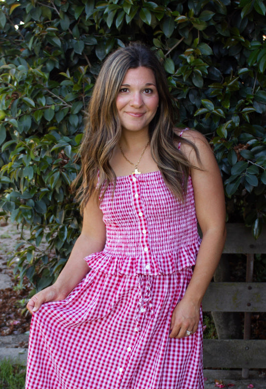 Woman wearing a pink checkered dress standing outdoors with greenery in the background