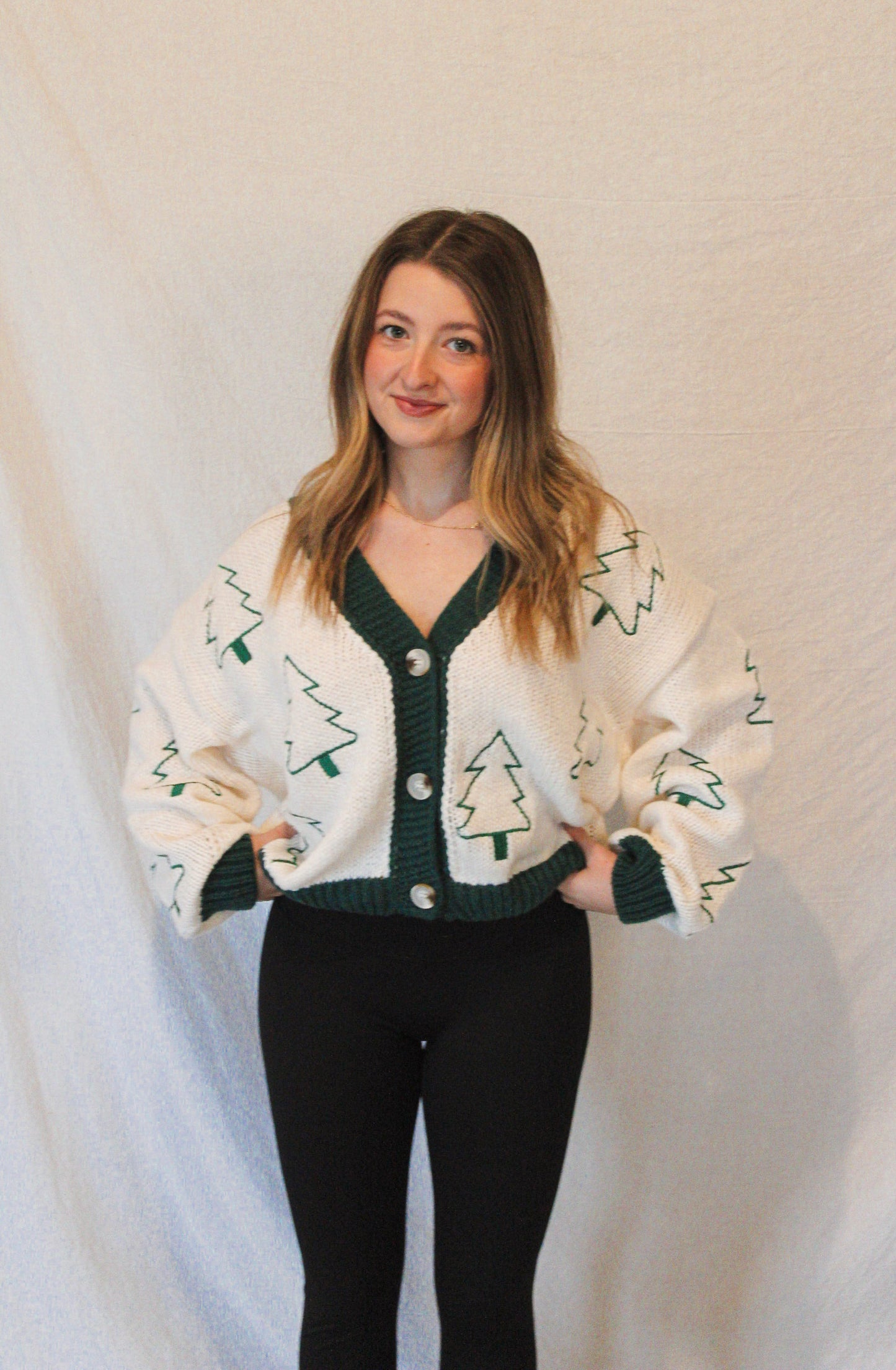 Person wearing a white cardigan with green tree patterns on a plain background