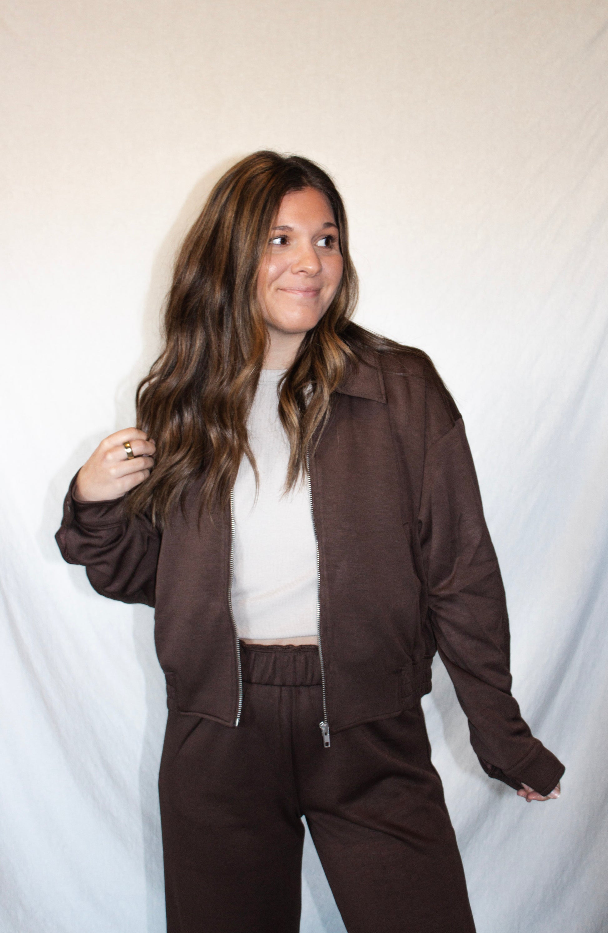 Woman wearing a brown jacket and pants set against a plain background