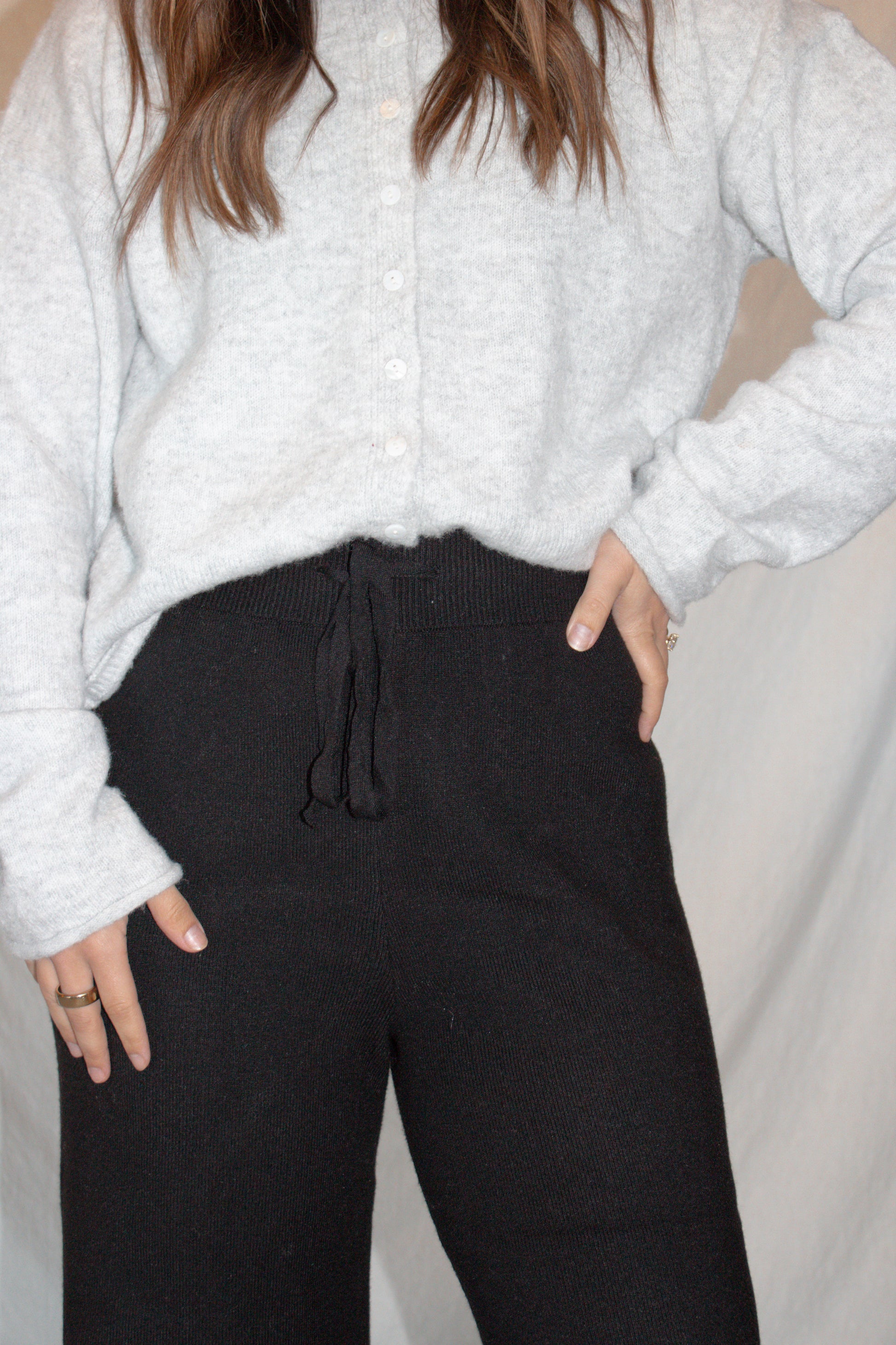 Person wearing a light gray textured sweater and black pants against a neutral background