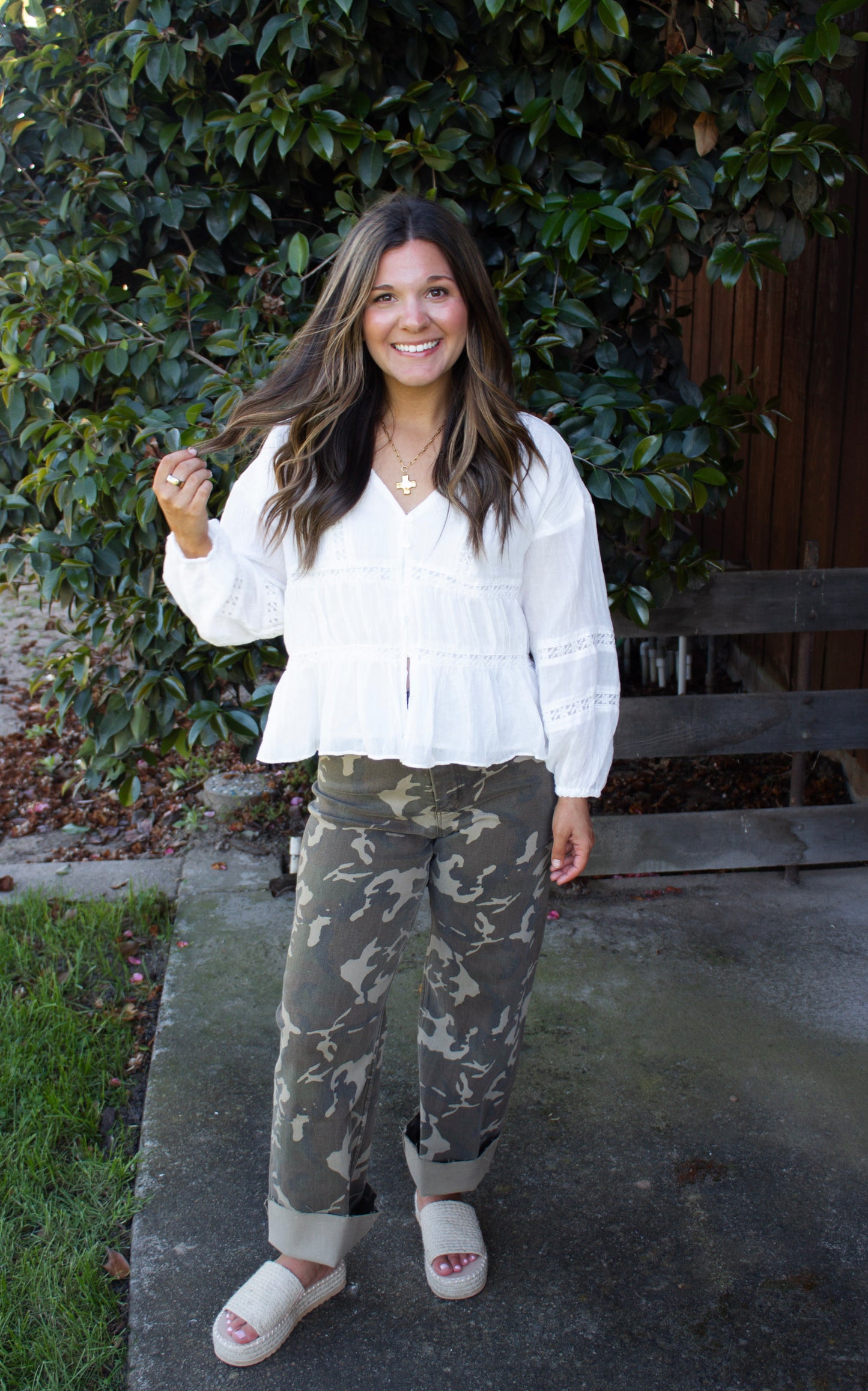 Woman wearing a white blouse and camouflage pants standing outdoors.