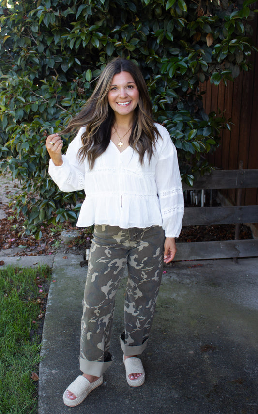 Woman wearing a white blouse and camouflage pants standing outdoors.