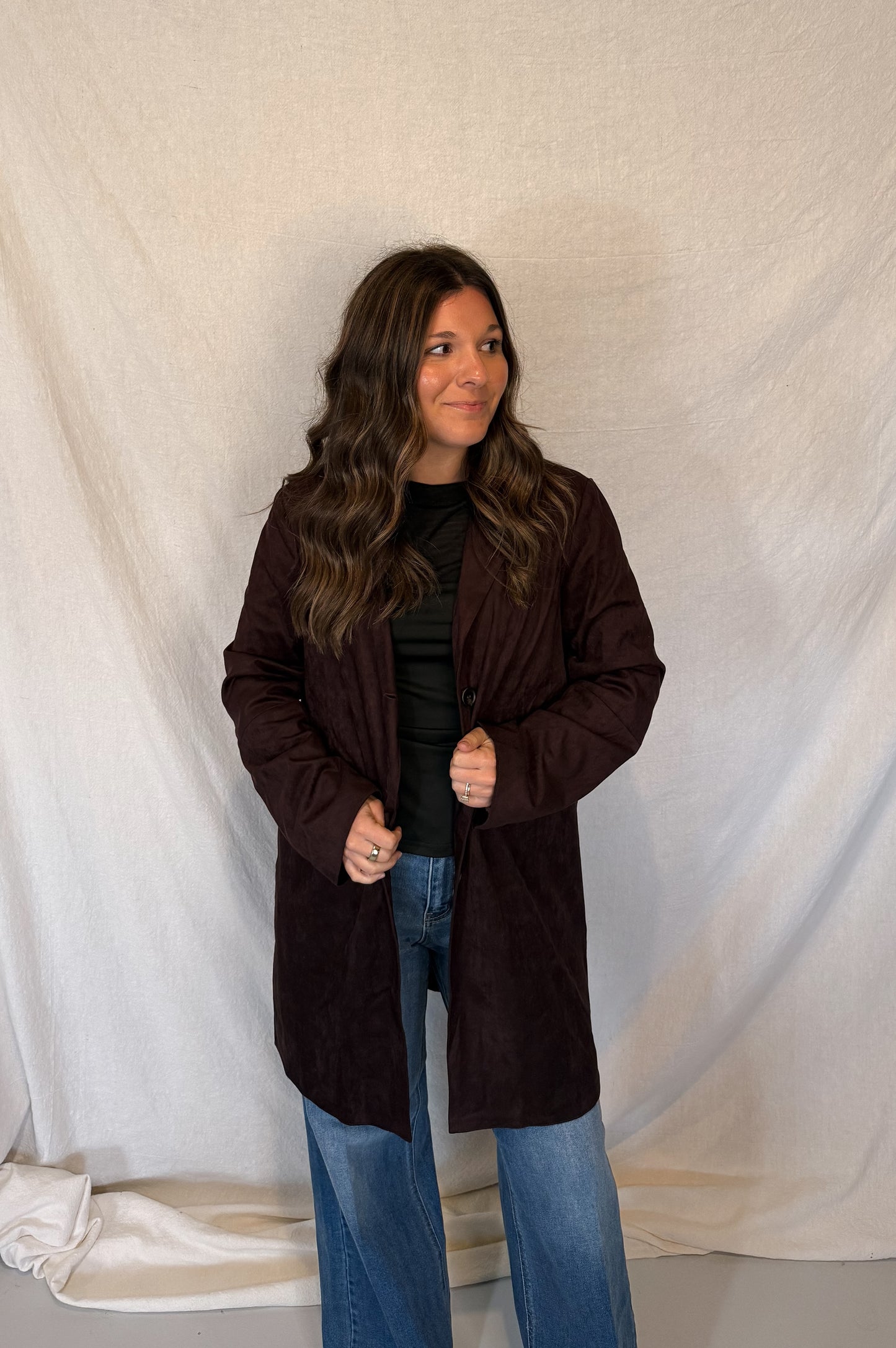 Woman wearing a brown coat standing against a white curtain