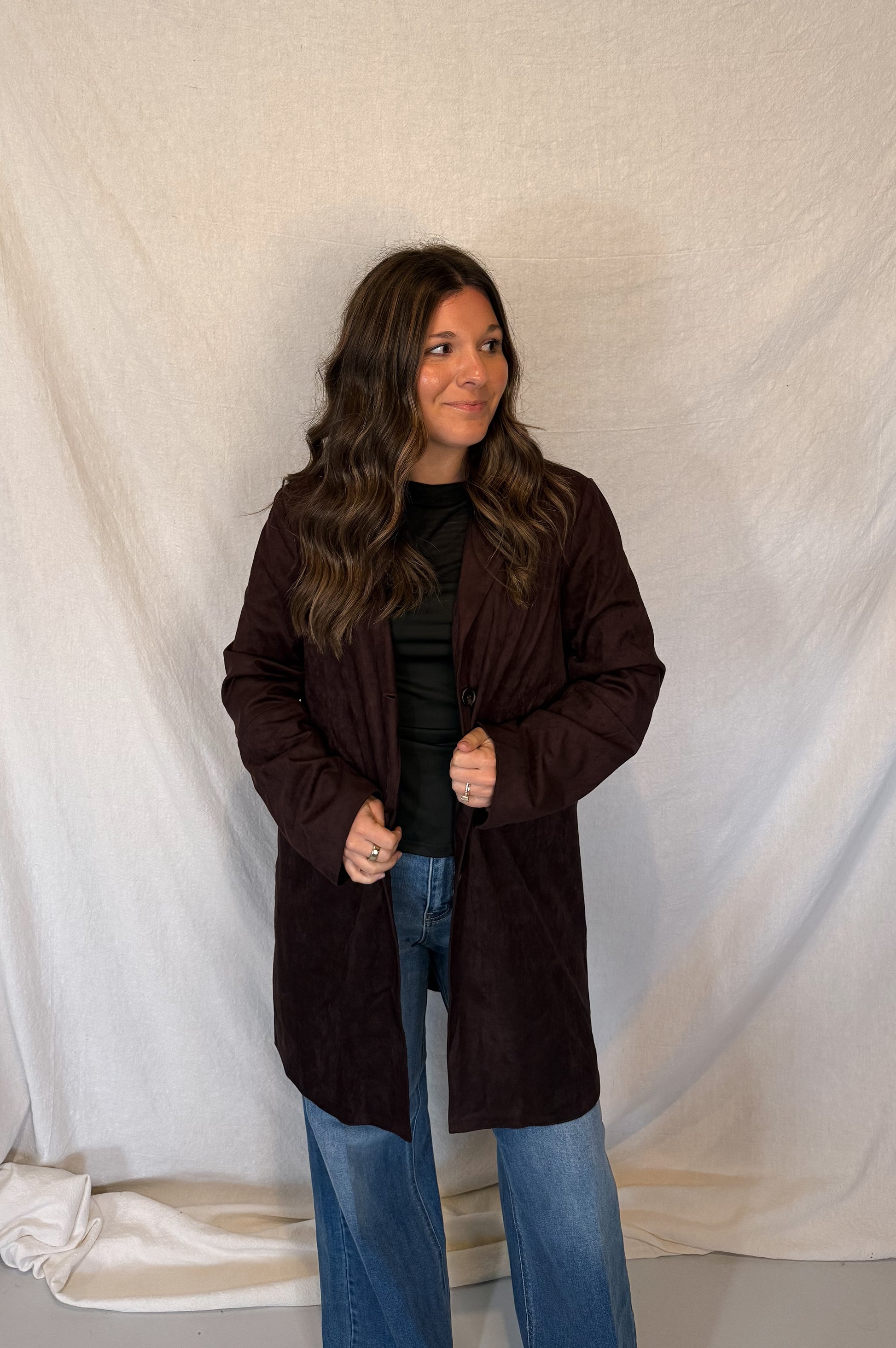 Woman wearing a brown coat standing against a white curtain