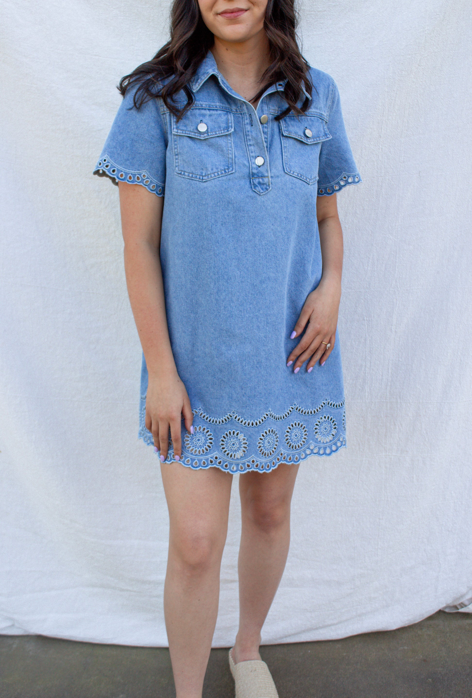 Woman wearing a blue denim dress with lace trim against a white background