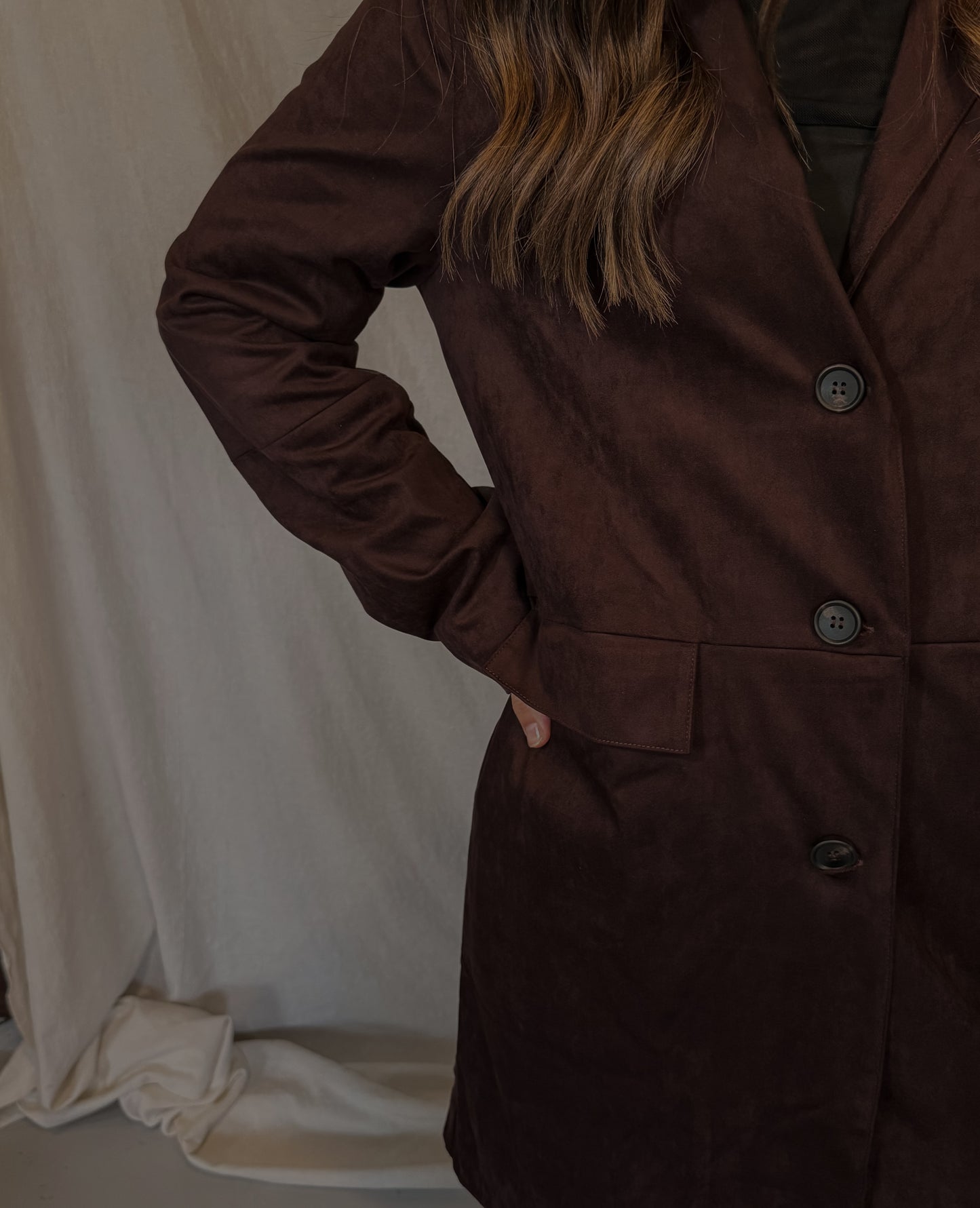 Brown coat worn by a person against a white curtain background