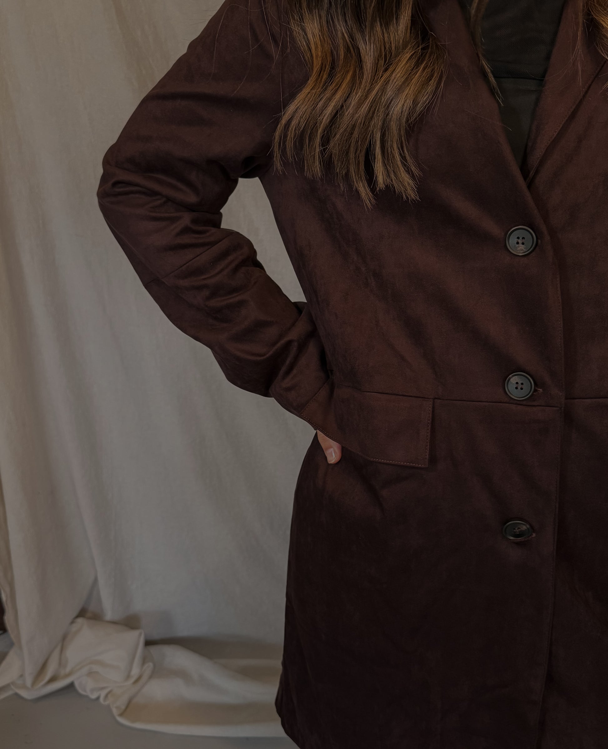 Brown coat worn by a person against a white curtain background