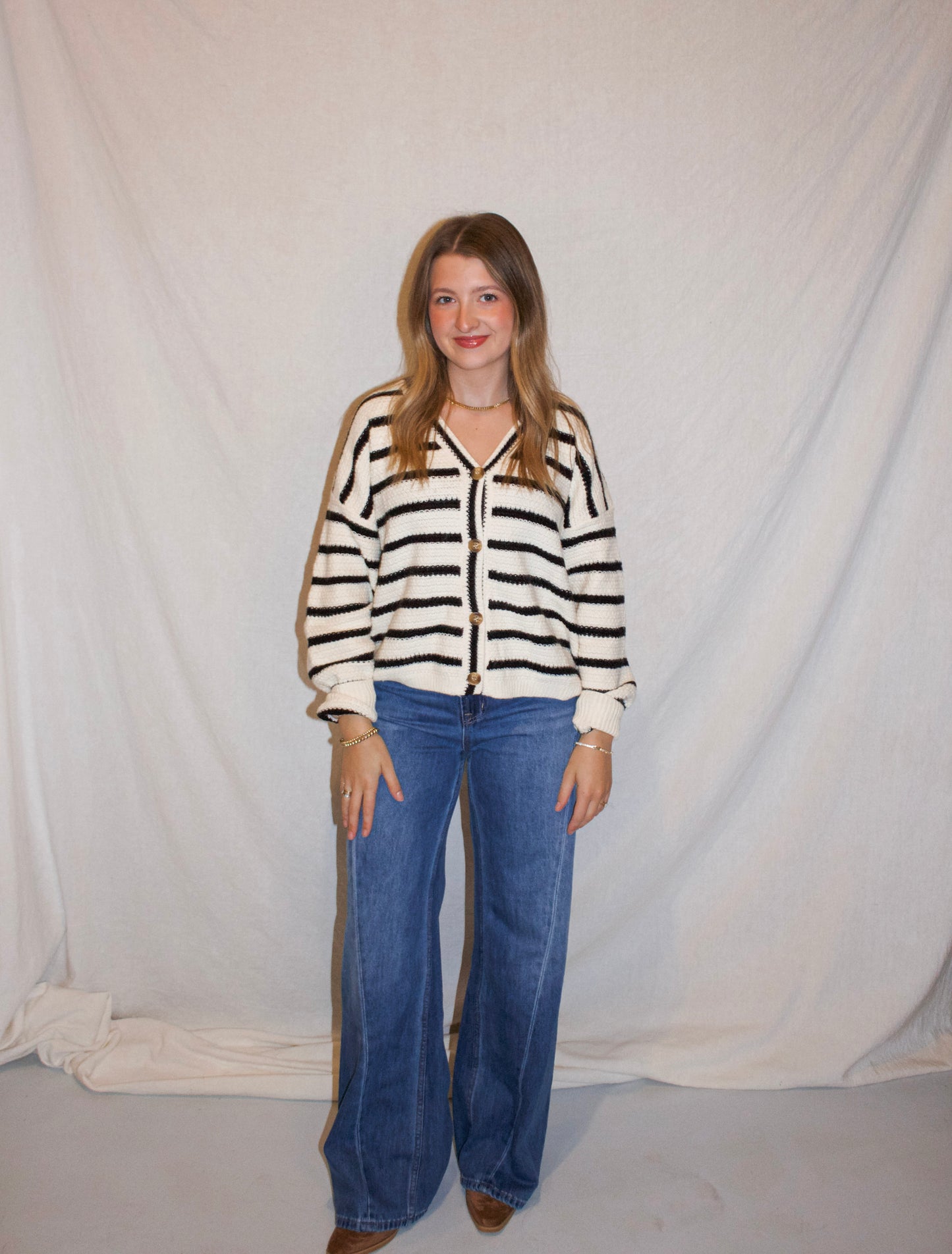 Person wearing a striped sweater and blue jeans against a plain background