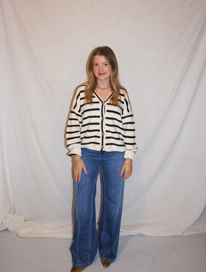Person wearing a striped sweater and blue jeans against a plain background