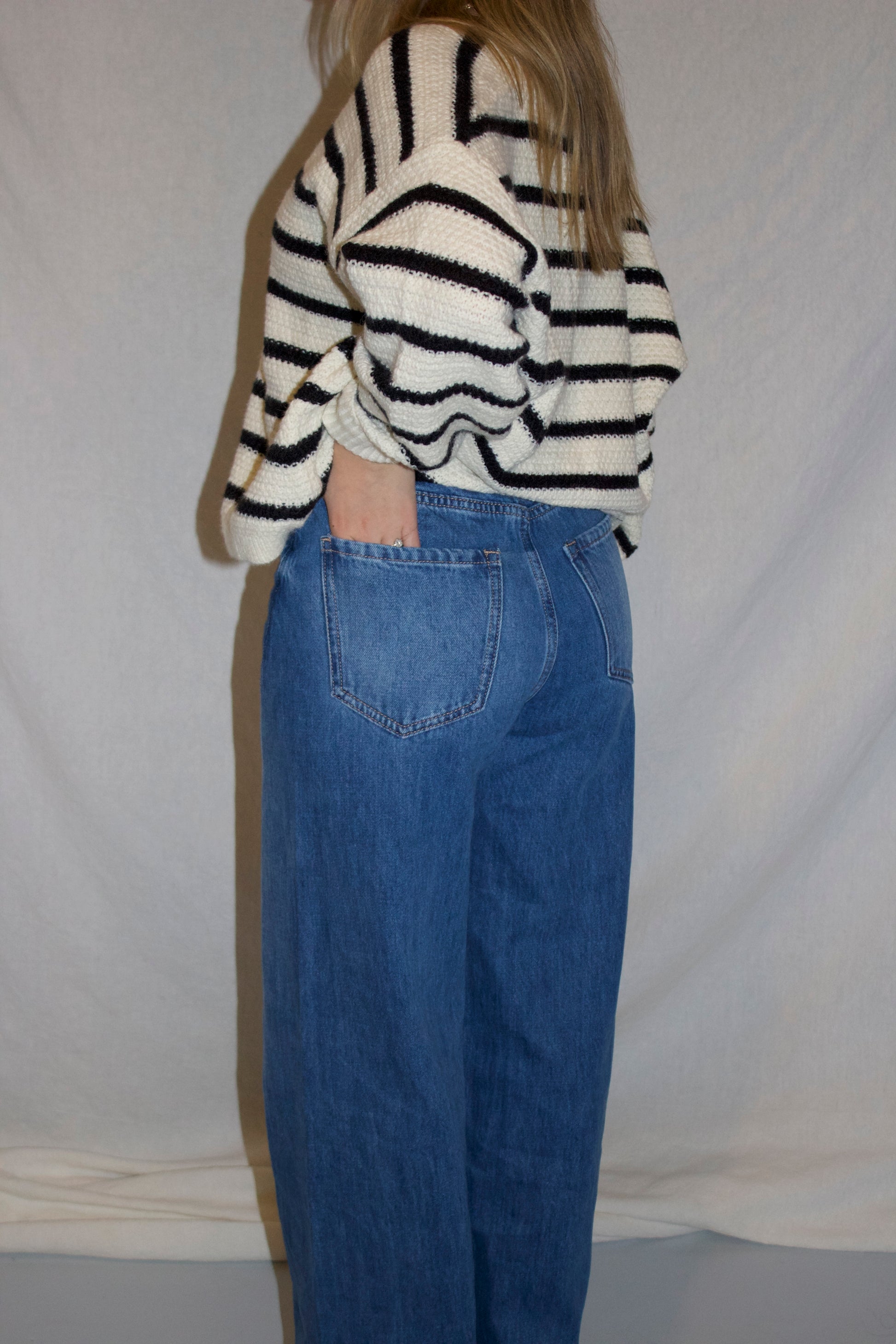 Person wearing a striped sweater and blue jeans against a plain background