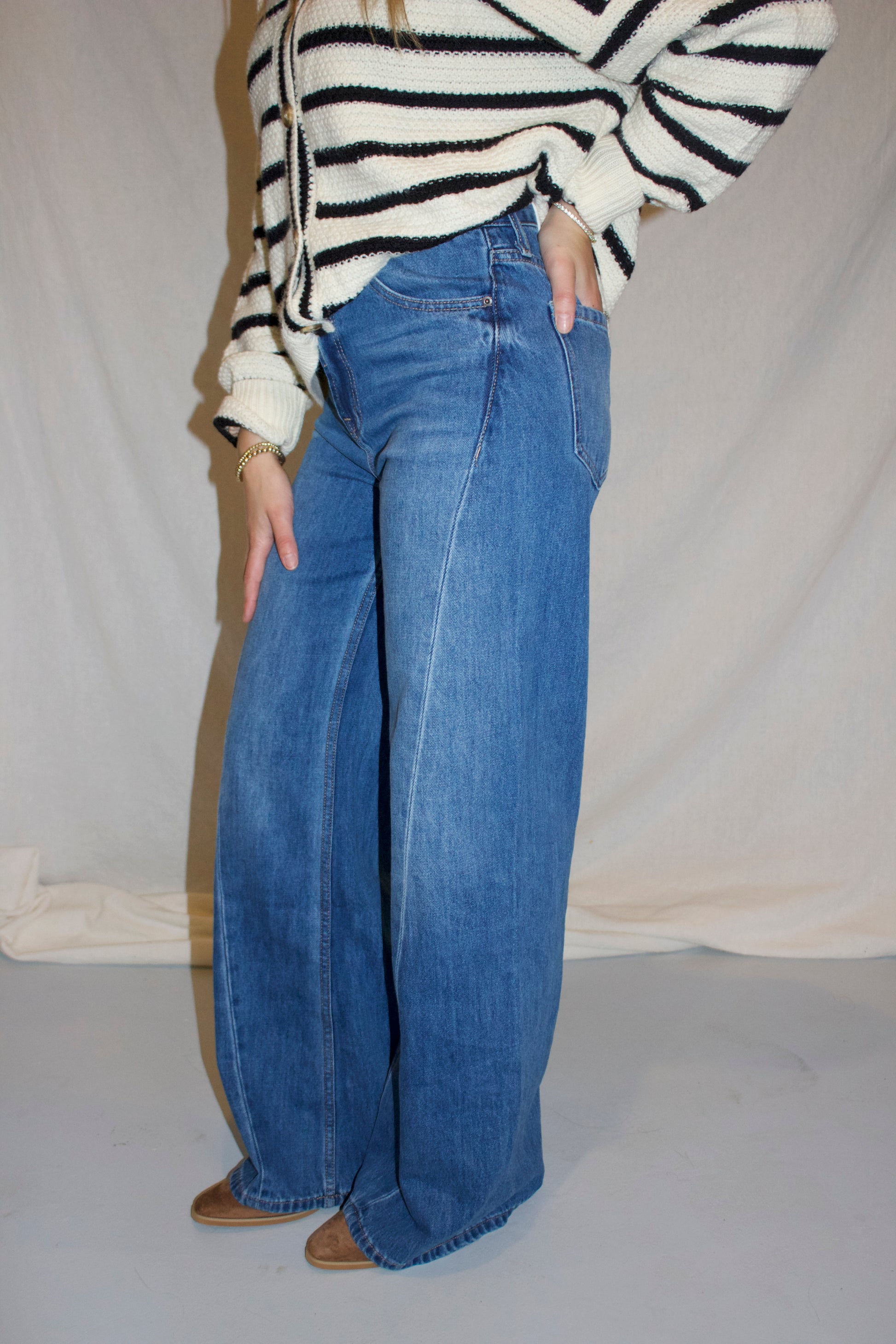 Person wearing a striped sweater and blue jeans against a plain background