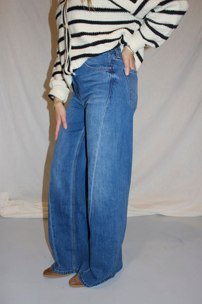 Person wearing a striped sweater and blue jeans against a plain background