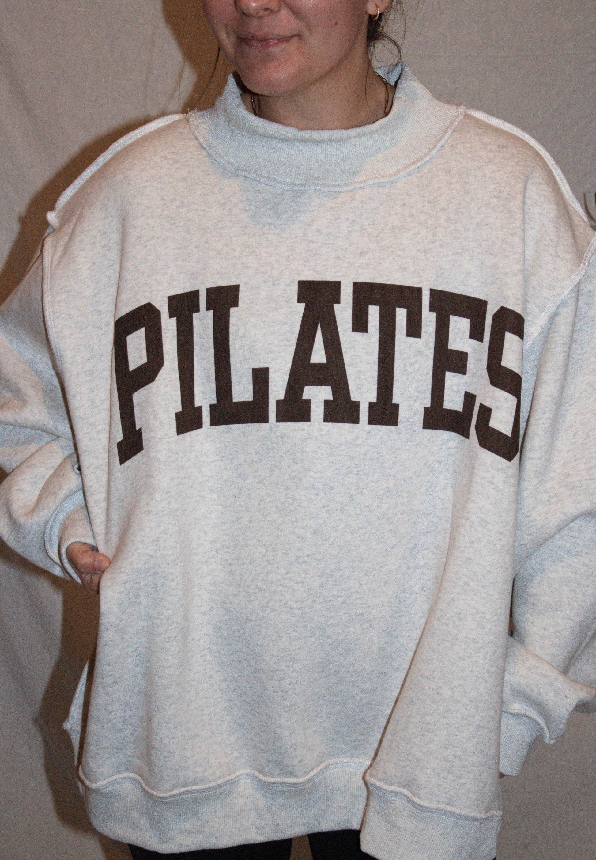Person wearing a gray sweatshirt with 'PILATES' printed on it.