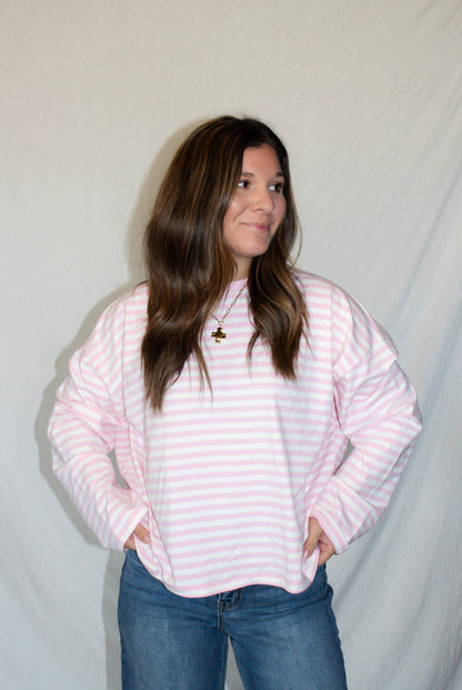 Person wearing a pink and white striped sweater and blue jeans against a plain background