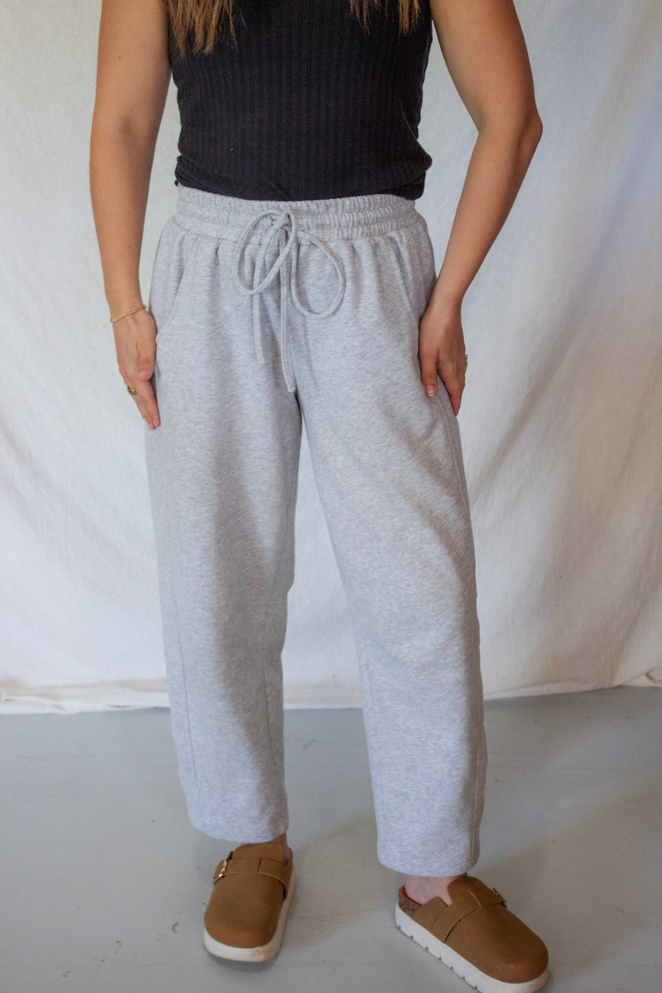 Person wearing gray sweatpants and brown shoes on a plain background