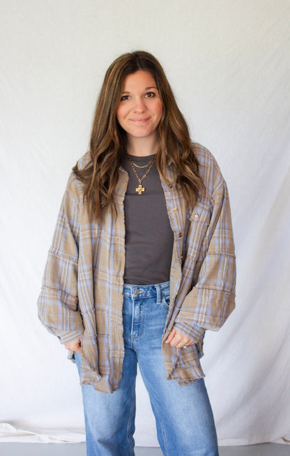 Woman wearing a plaid shirt over a gray top and blue jeans against a white background