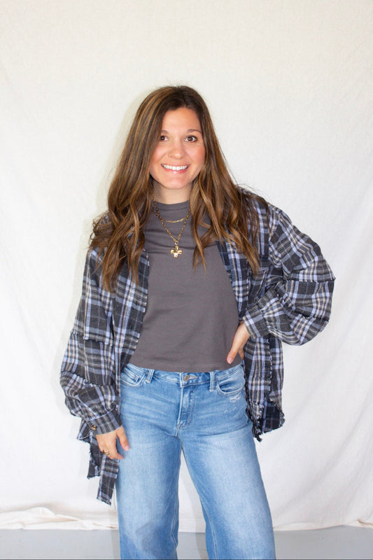 Woman wearing a plaid shirt, gray top, and blue jeans against a white background